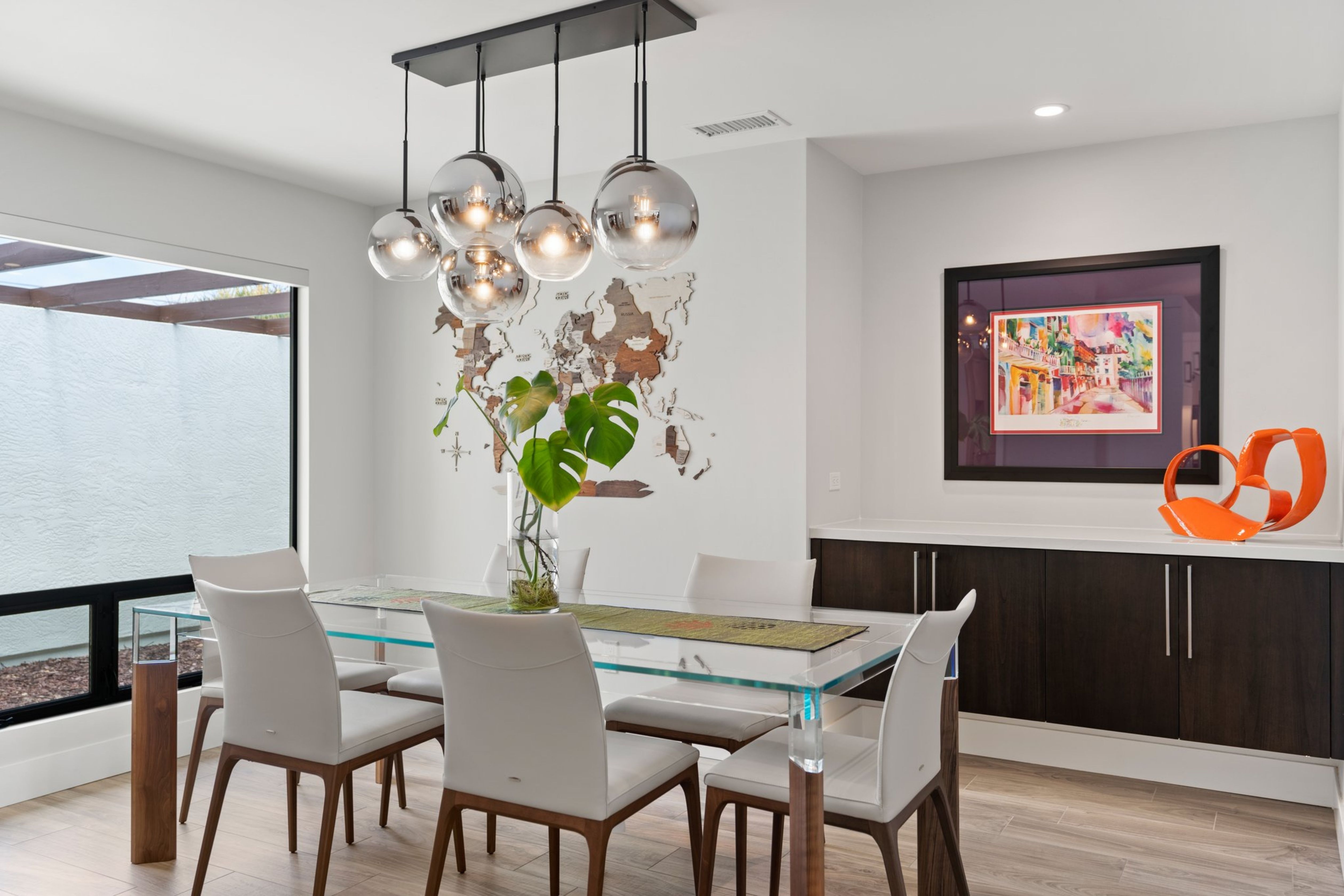 Dining area with globe pendant lights, dark built-in cabinetry, large window and light wood-look flooring.