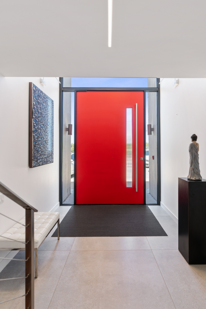 Entry foyer with red pivot door, glass sidelights, tile flooring, cable stair railing and linear ceiling lighting.