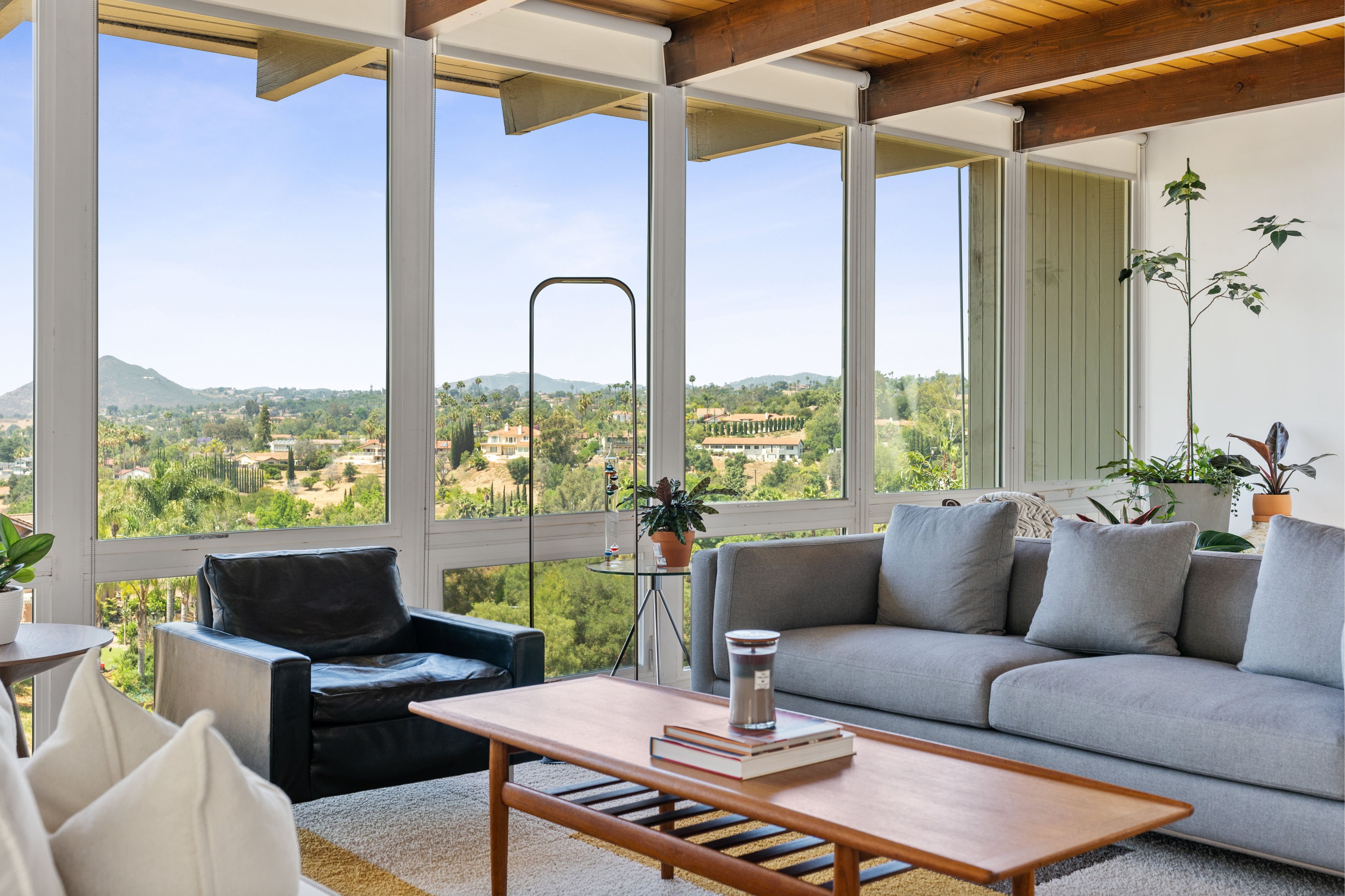 Living room with floor-to-ceiling windows, exposed wood beams, wood flooring and expansive hillside views.