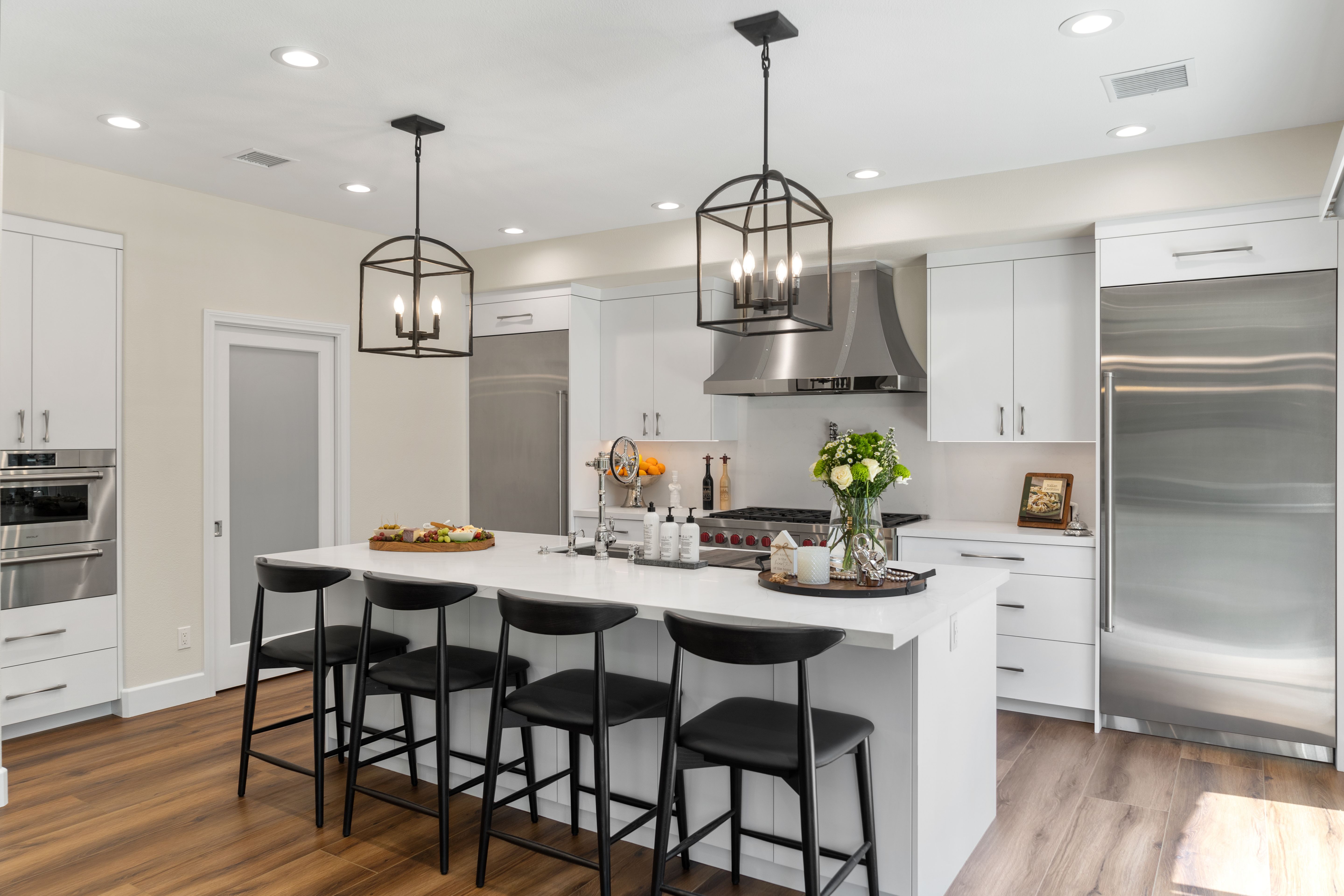 Remodeled kitchen with white cabinetry, large island, stainless appliances, lantern pendants and wood-look flooring.