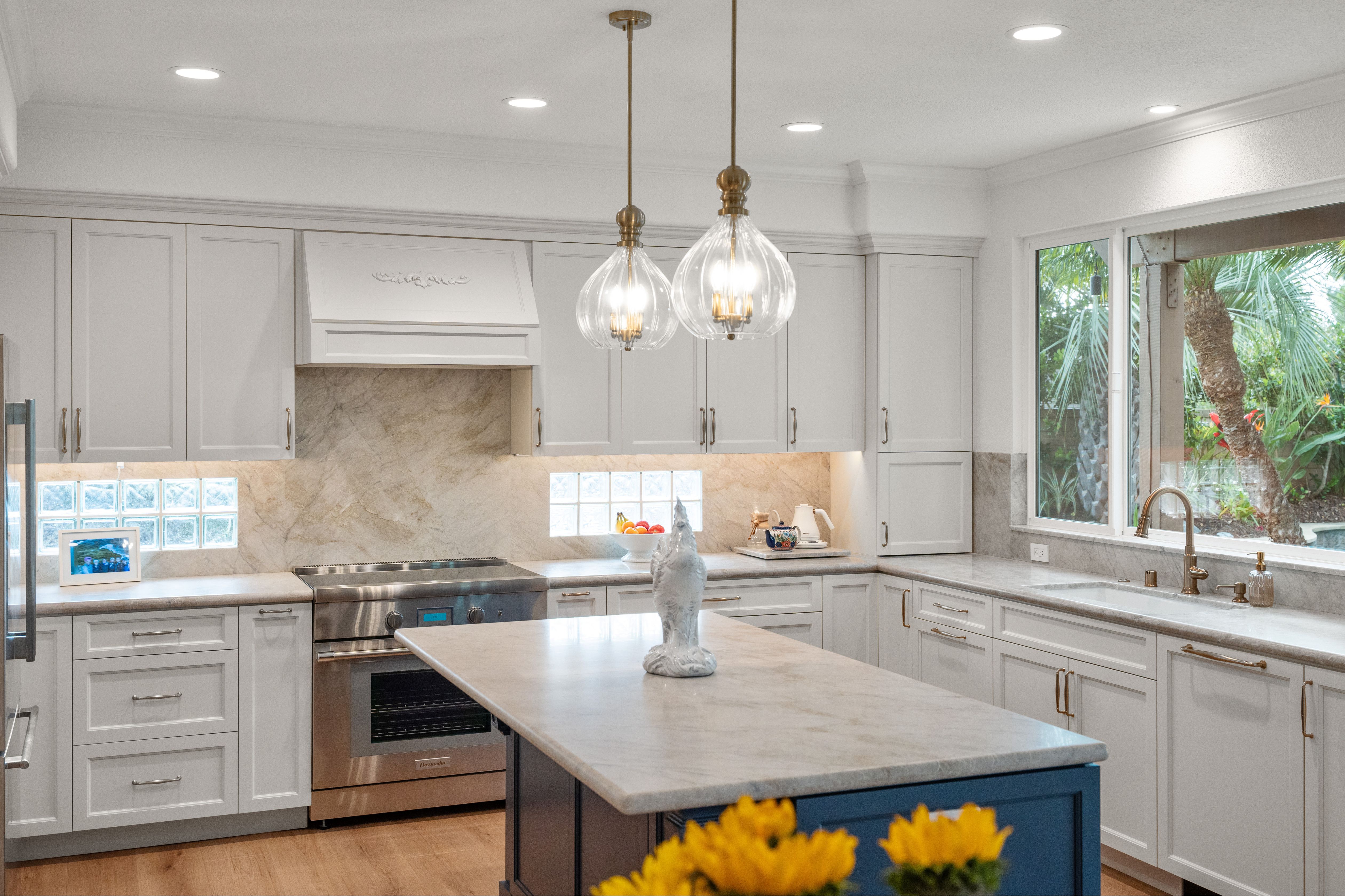Light kitchen with white cabinetry, blue island, stone counters, glass-block windows and brass accents.