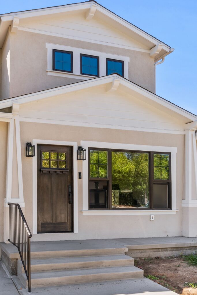 Front entry with dark wood door, black-framed windows, stucco exterior and layered gable rooflines