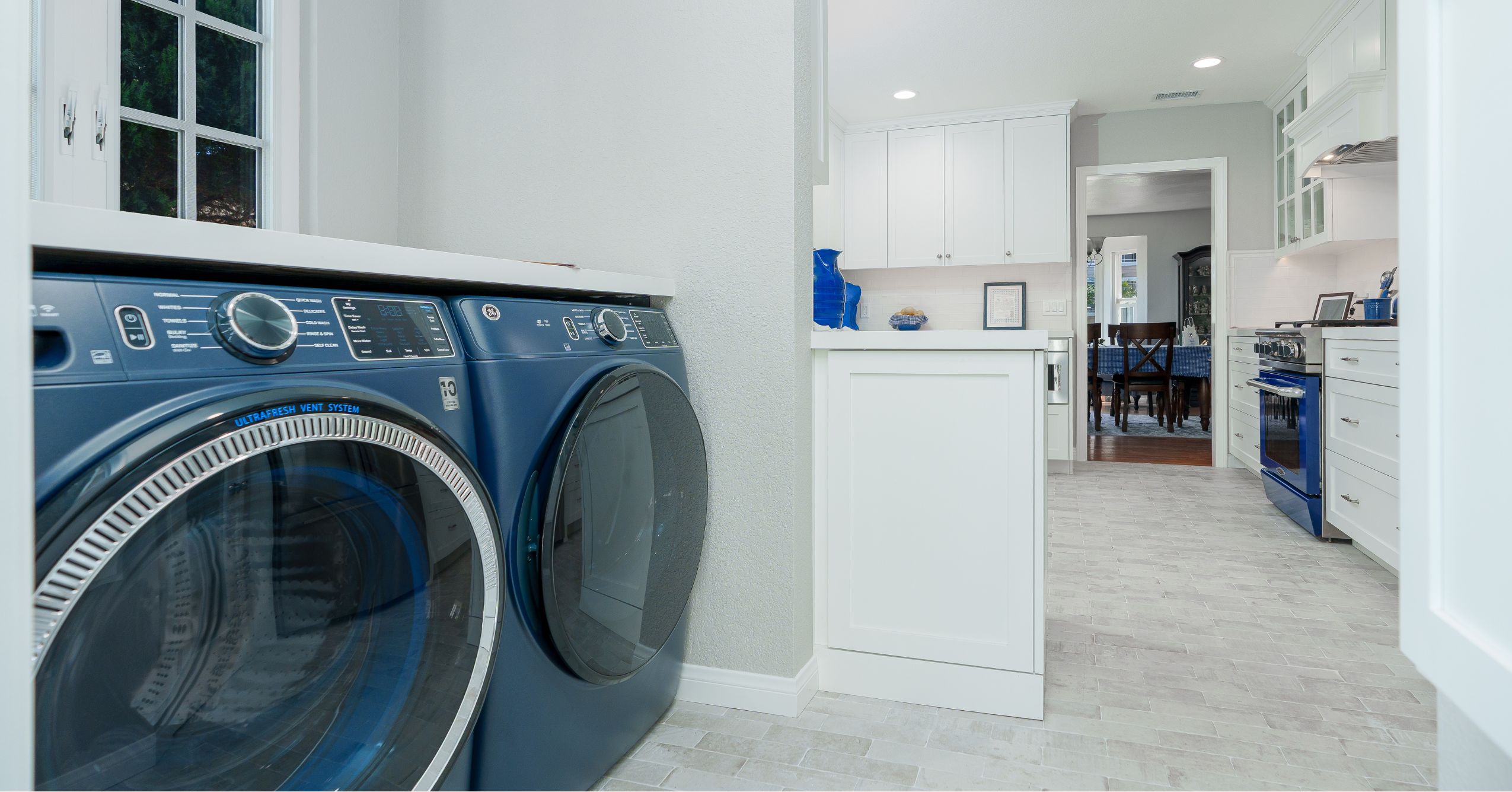 Adjacent laundry nook with blue front-load washer and dryer opening directly into the remodeled white kitchen.