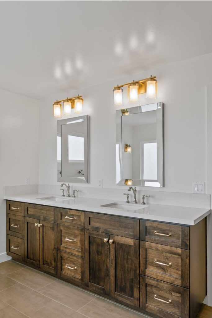 Primary bathroom double vanity with dark wood cabinetry, white countertop, framed mirrors and brass-tone vanity lights.