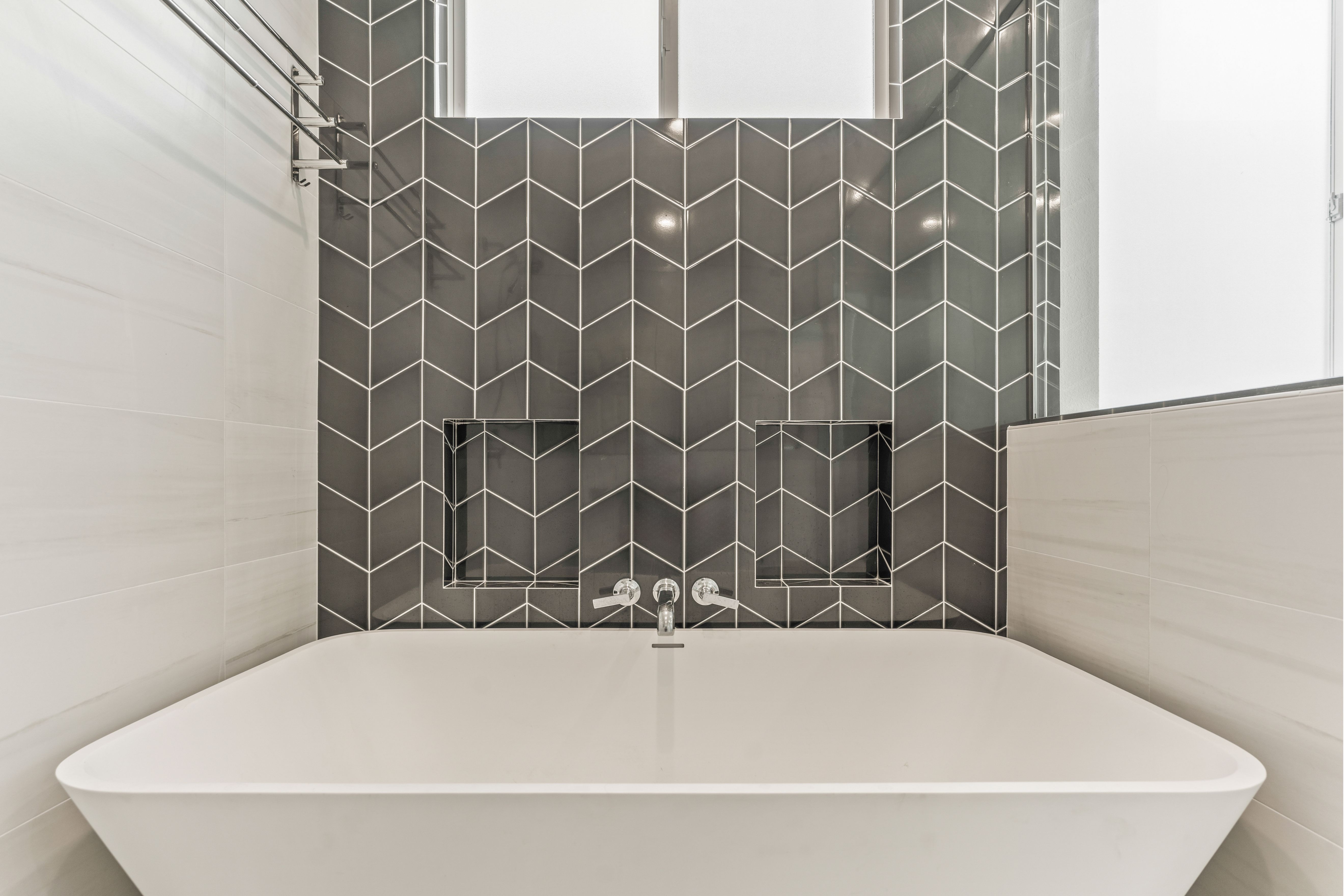 Freestanding tub with charcoal chevron tile, recessed niches, wall-mounted faucet and frosted window.