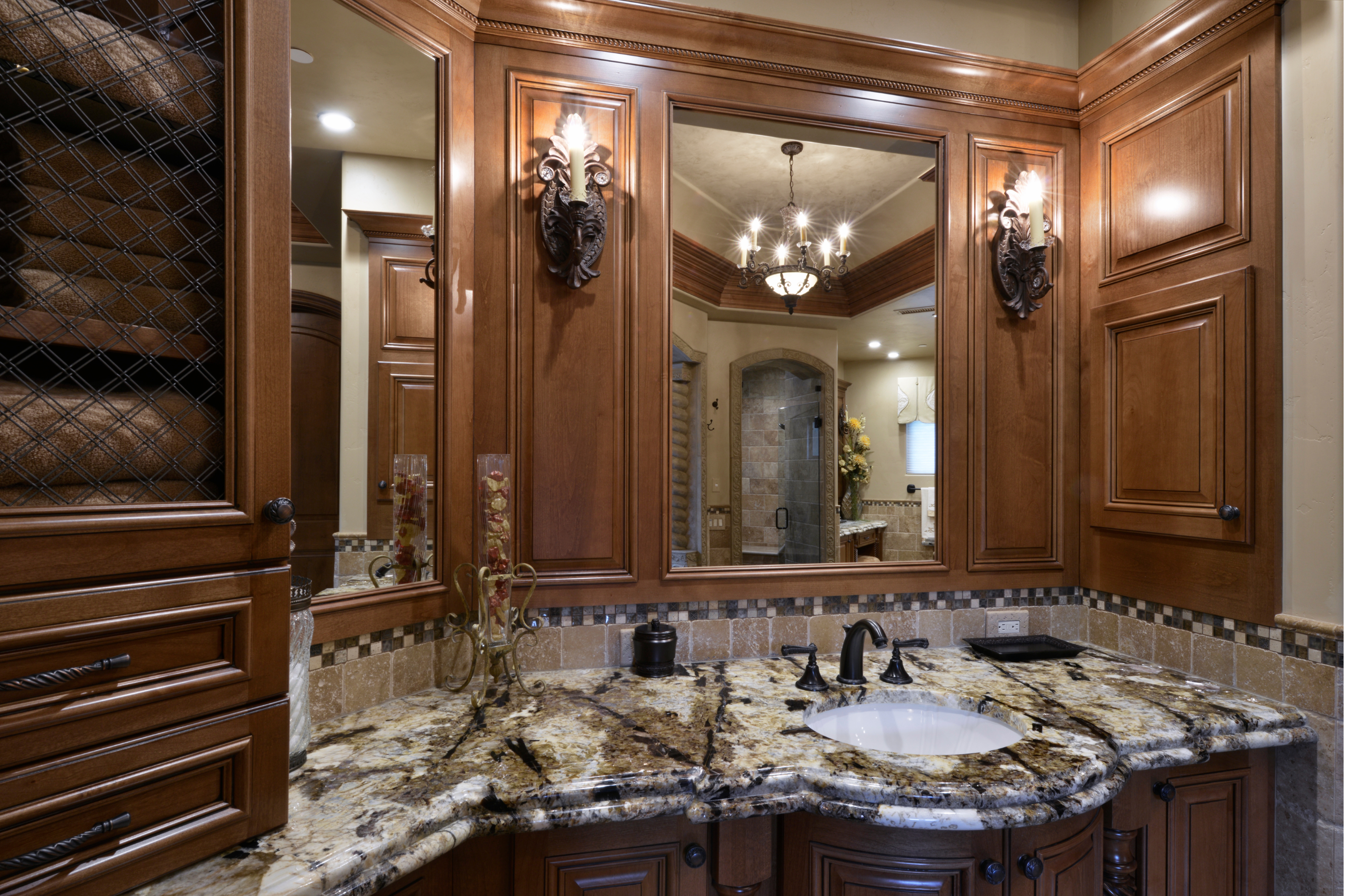 Custom wood bathroom vanity with stone countertop, inset sink, framed mirrors and decorative wall sconces.