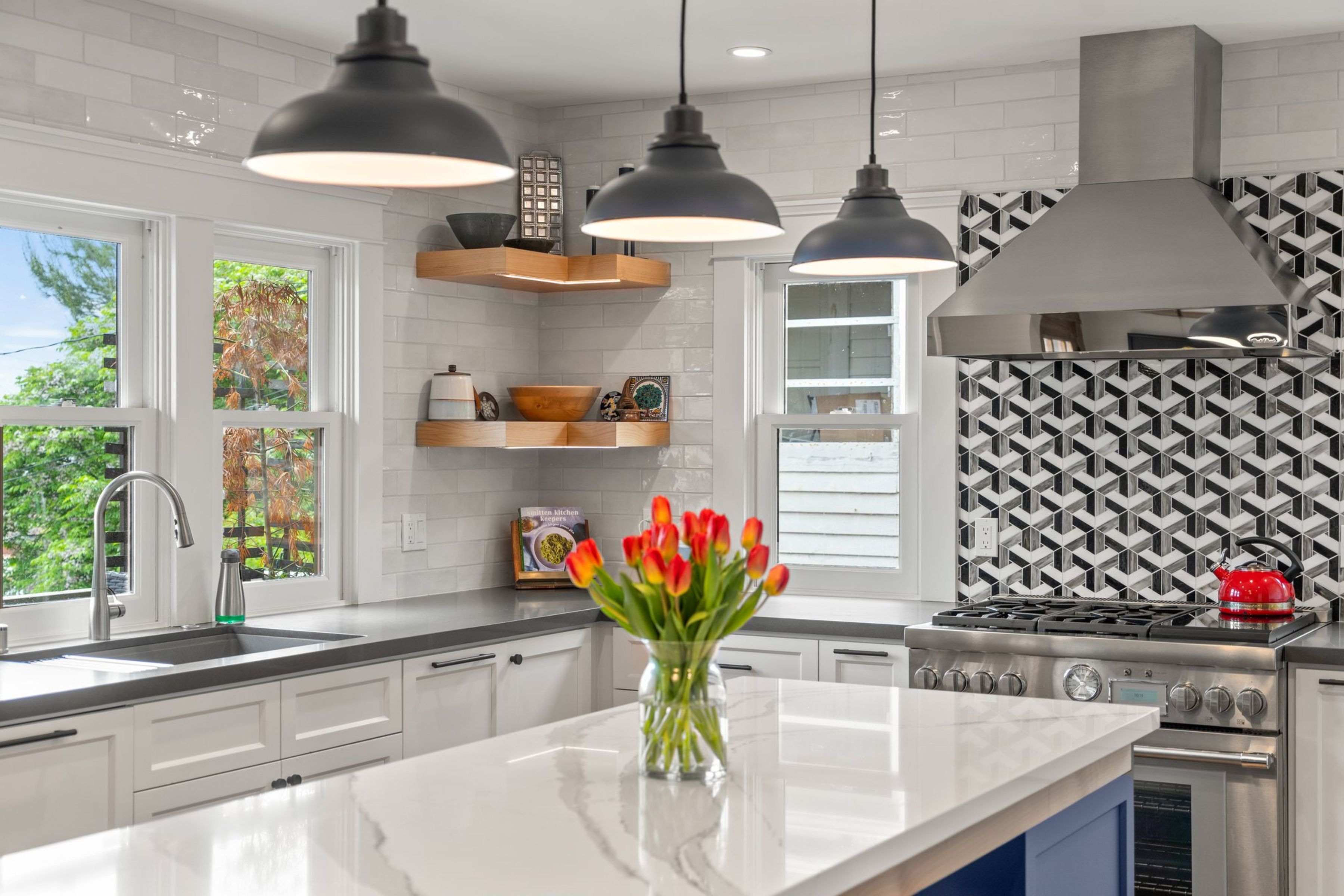Kitchen cooking wall with stainless range and hood, geometric backsplash, white cabinetry and wood floating shelves.