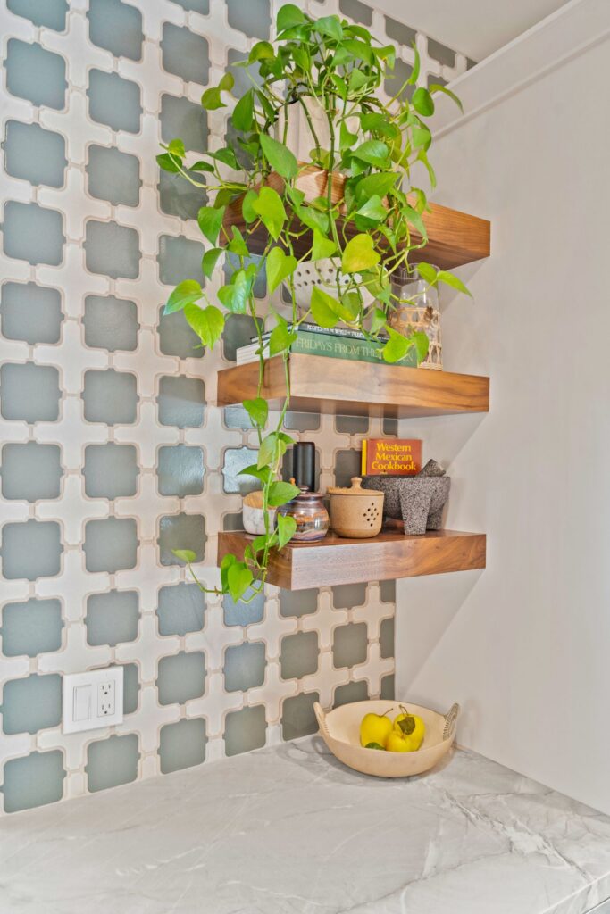 Kitchen corner with green patterned tile backsplash, wood floating shelves, stone countertop and trailing plant