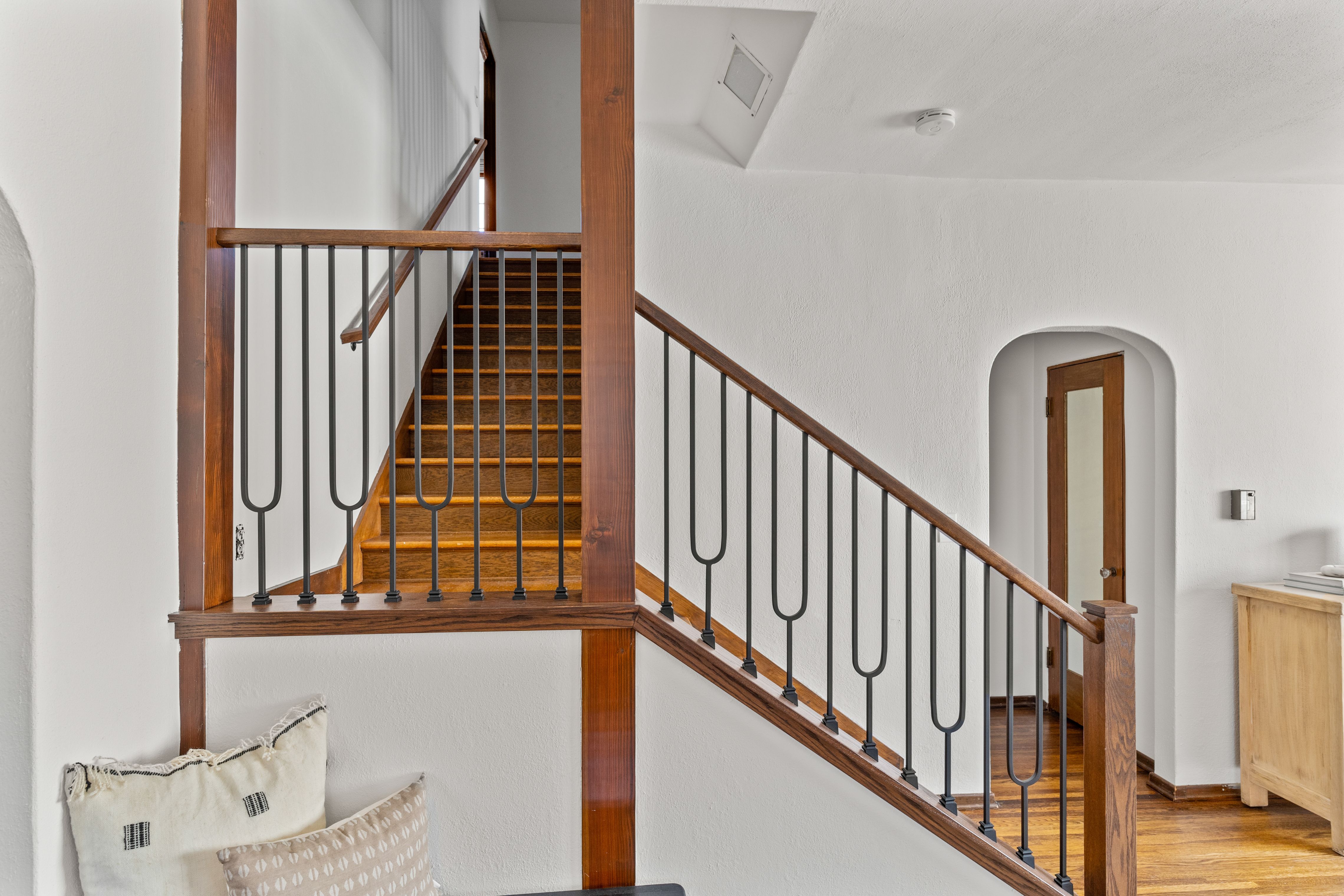 Wood staircase and landing with black metal railings, exposed wood posts and an arched doorway.