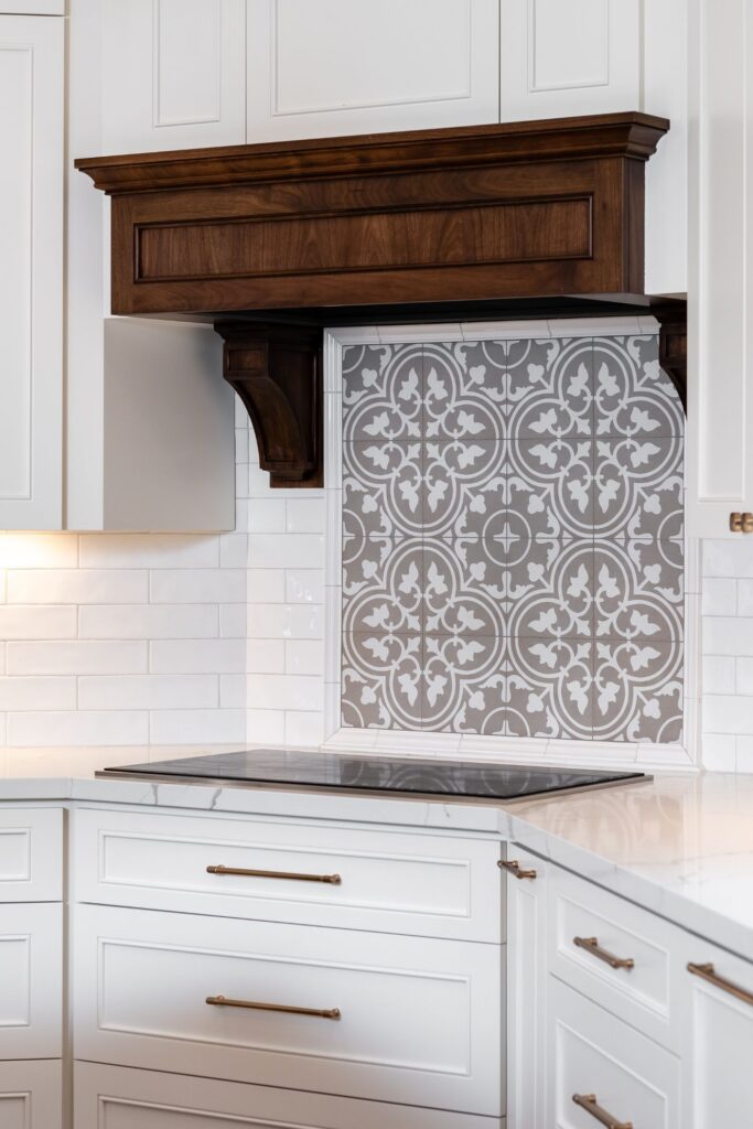 Cooktop wall with white cabinetry, dark wood hood surround, patterned tile accent and veined countertop.