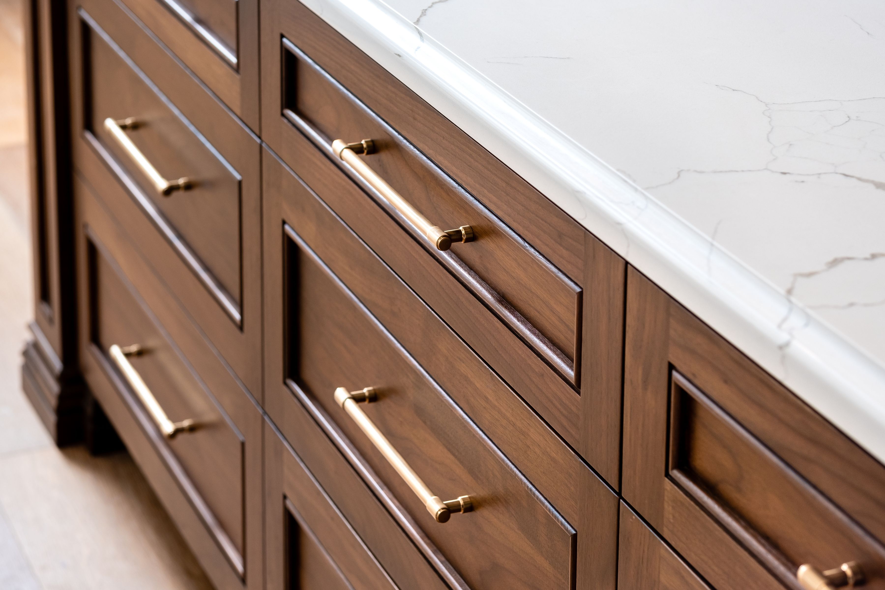 Wood kitchen island drawers with brass pulls and white veined quartz countertop.