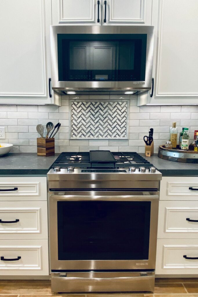 Stainless gas range and microwave framed by white cabinetry, subway tile and herringbone backsplash accent