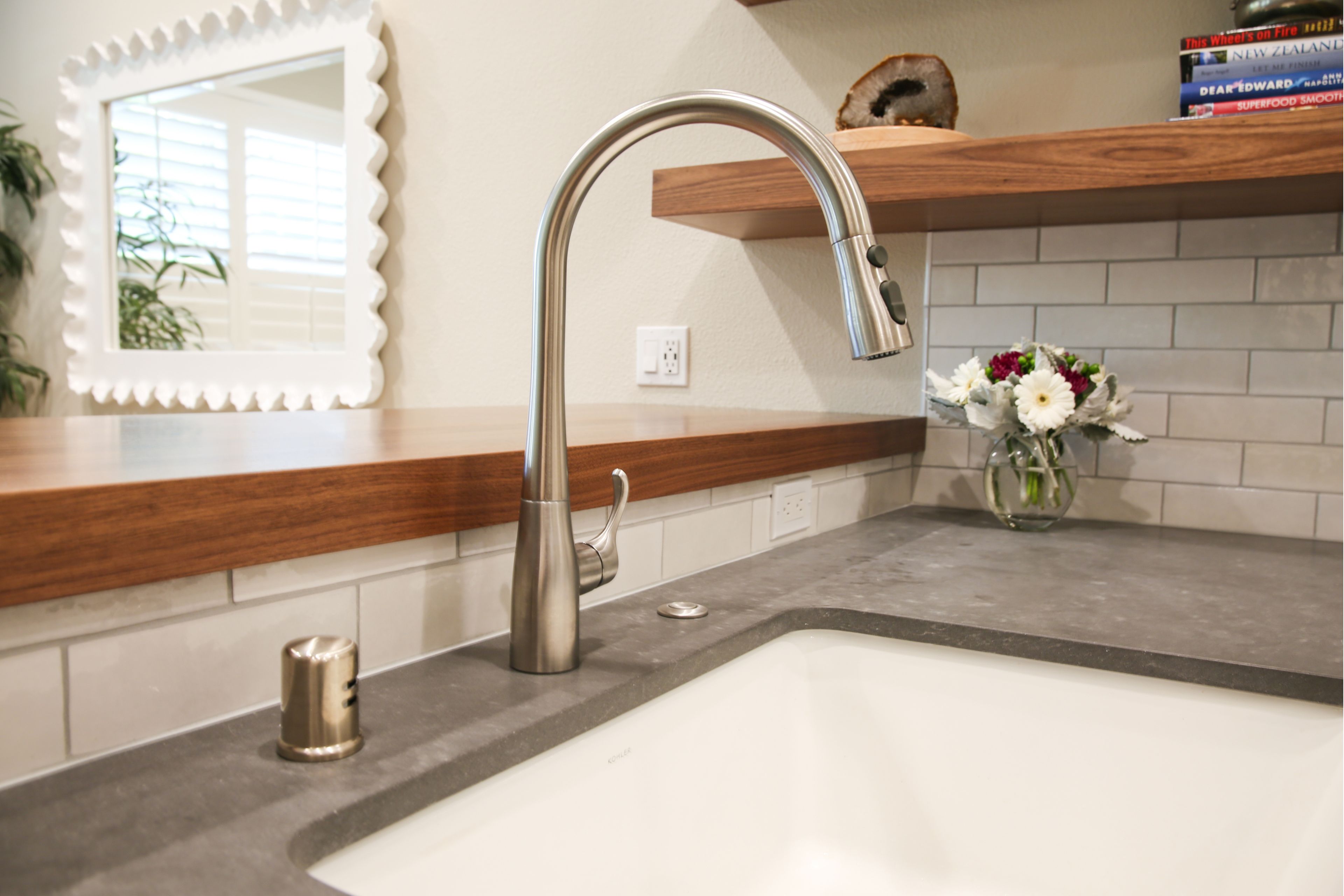 Apron-front kitchen sink with stainless faucet, gray countertop, subway tile and walnut floating shelves