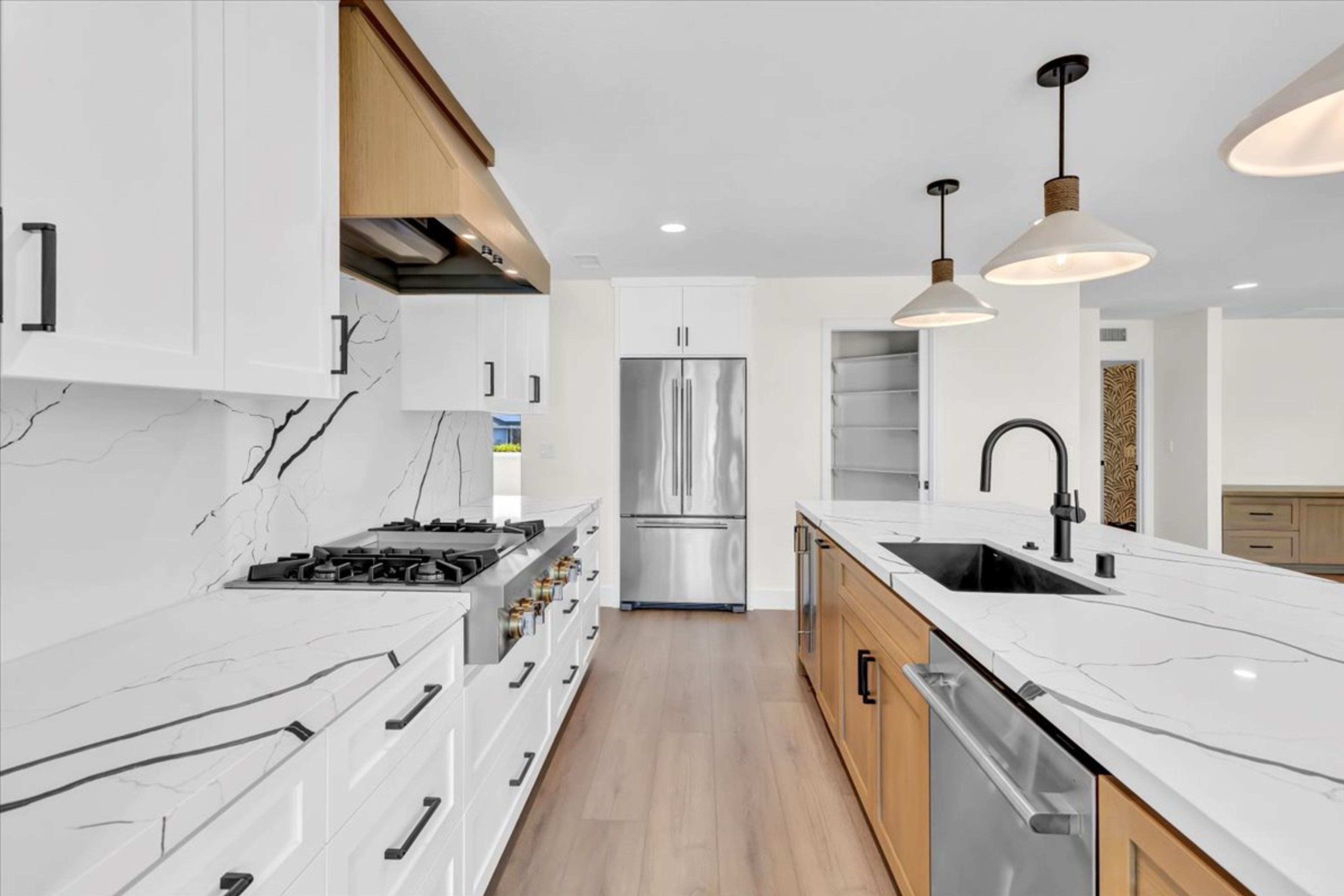 Remodeled kitchen with large island, white cabinetry, veined slab surfaces, black faucet, pendant lights and patio doors.