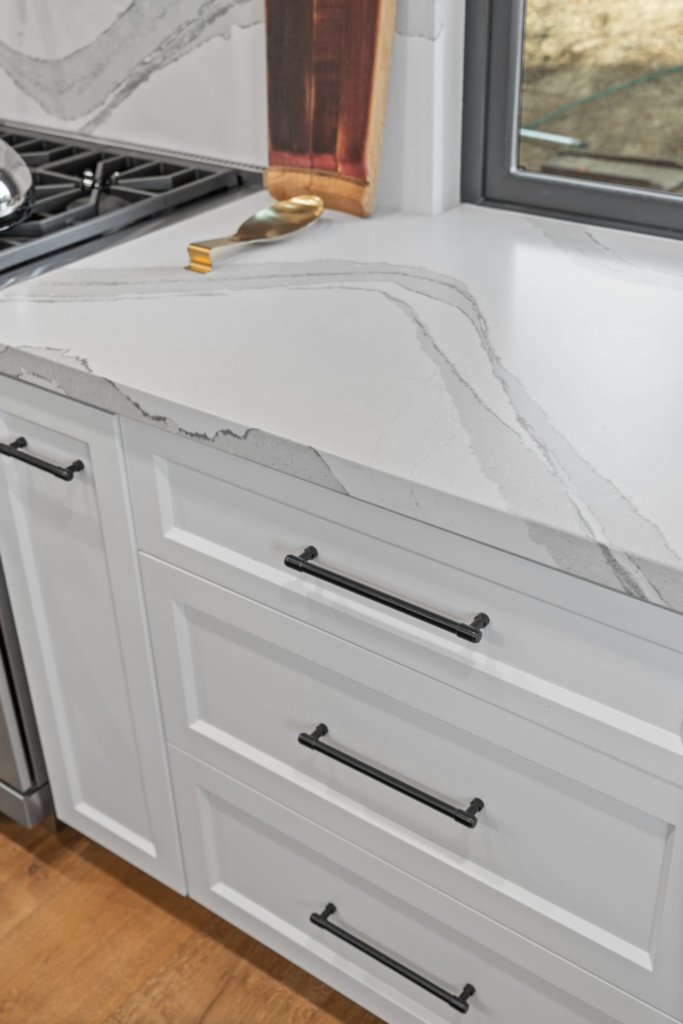 White shaker kitchen drawers with black pulls beneath a white veined countertop beside the cooking area.