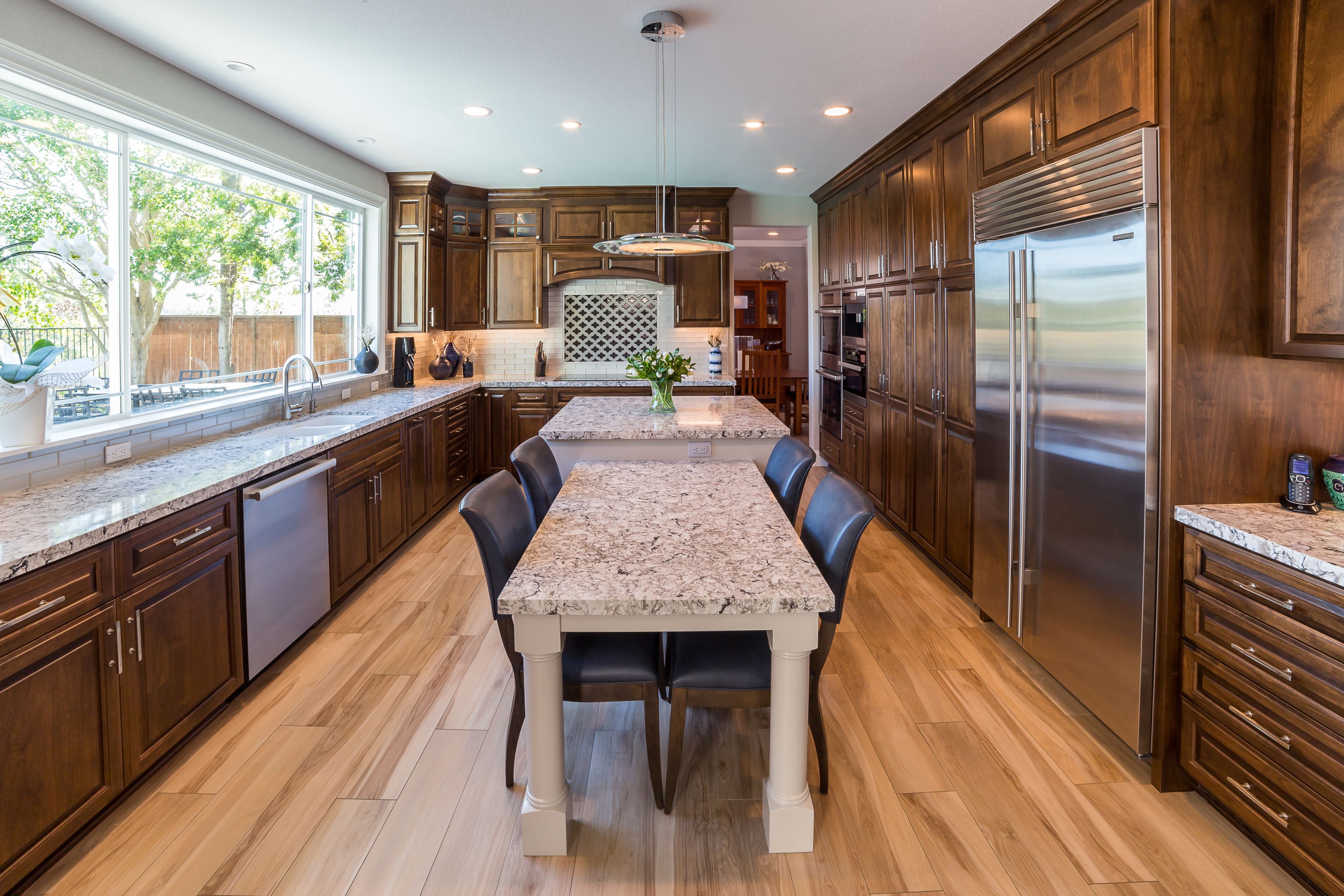 Encinitas kitchen with stained wood cabinetry, granite work surfaces, stainless appliances and large window.