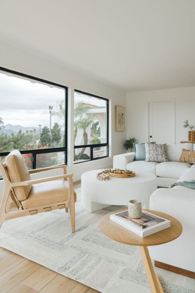 Living room with white sectional, tan lounge chair and large black-framed windows overlooking the landscape