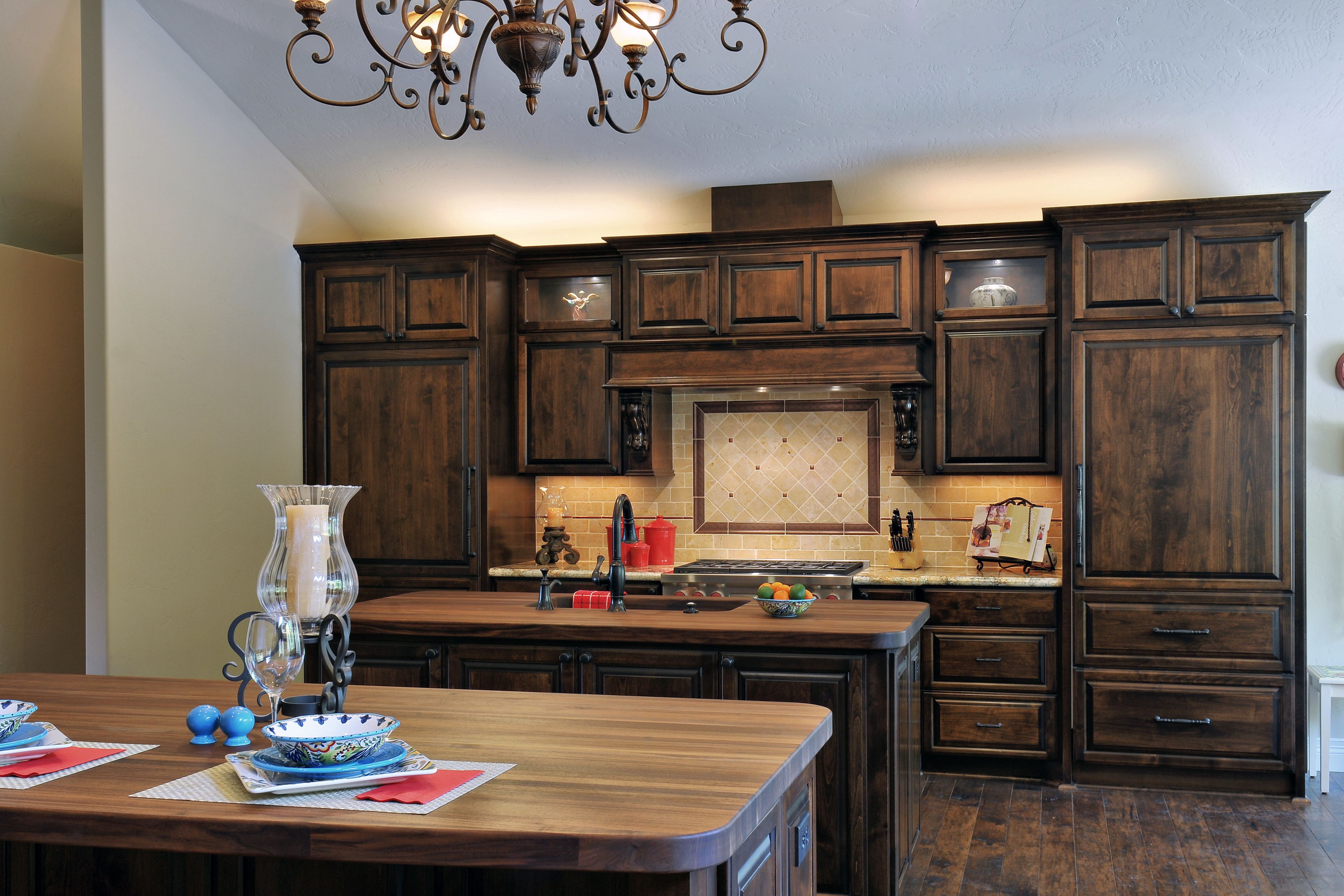 Two-island kitchen with dark alder cabinetry, walnut tops, vaulted ceiling and wrought-iron chandelier