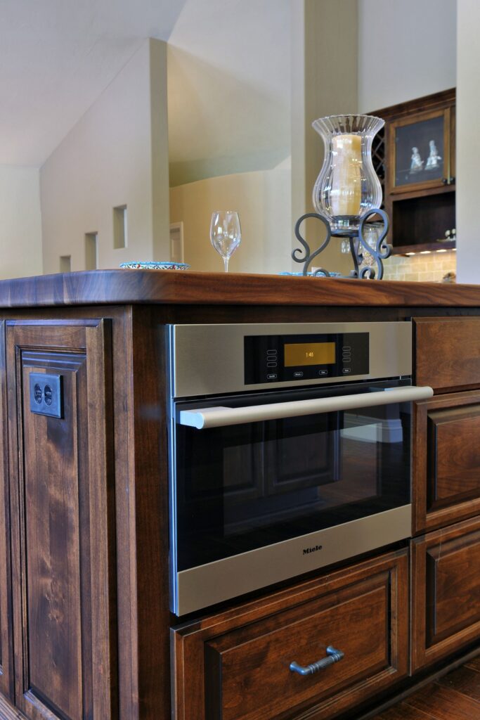 Built-in wall oven set into dark wood island cabinetry with thick walnut countertop and raised-panel detailing