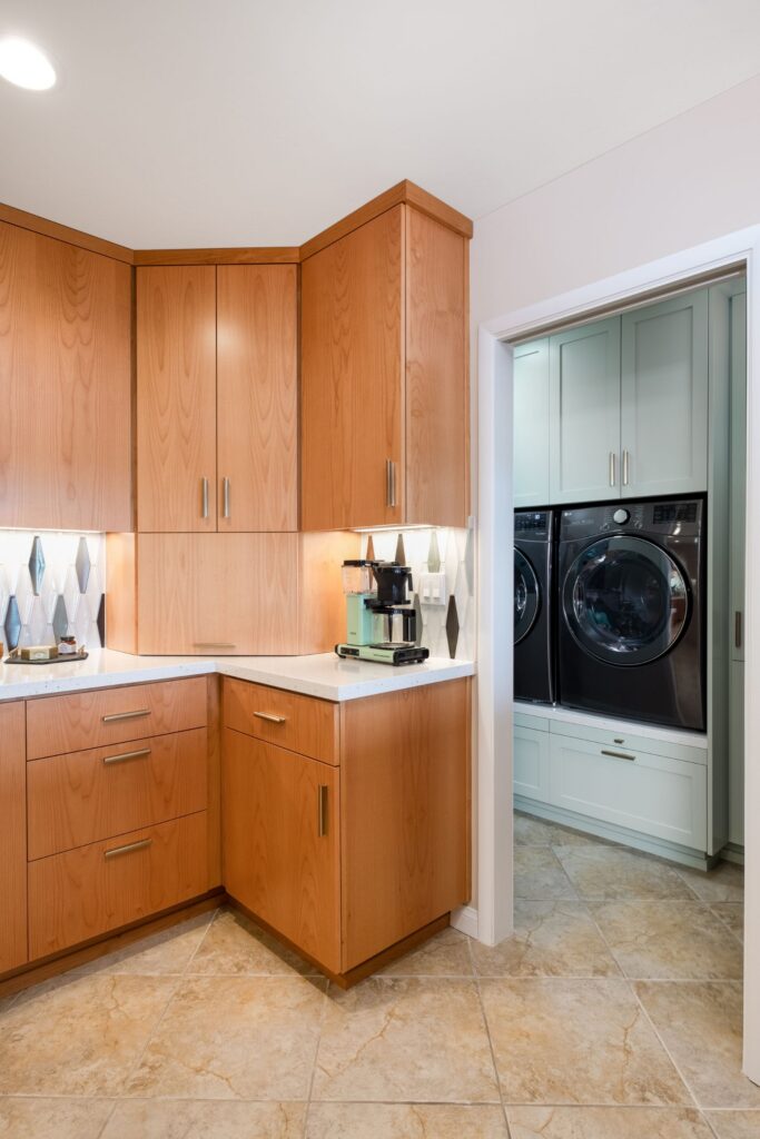 Kitchen corner with warm wood cabinetry, white countertops and doorway to mint-green laundry storage