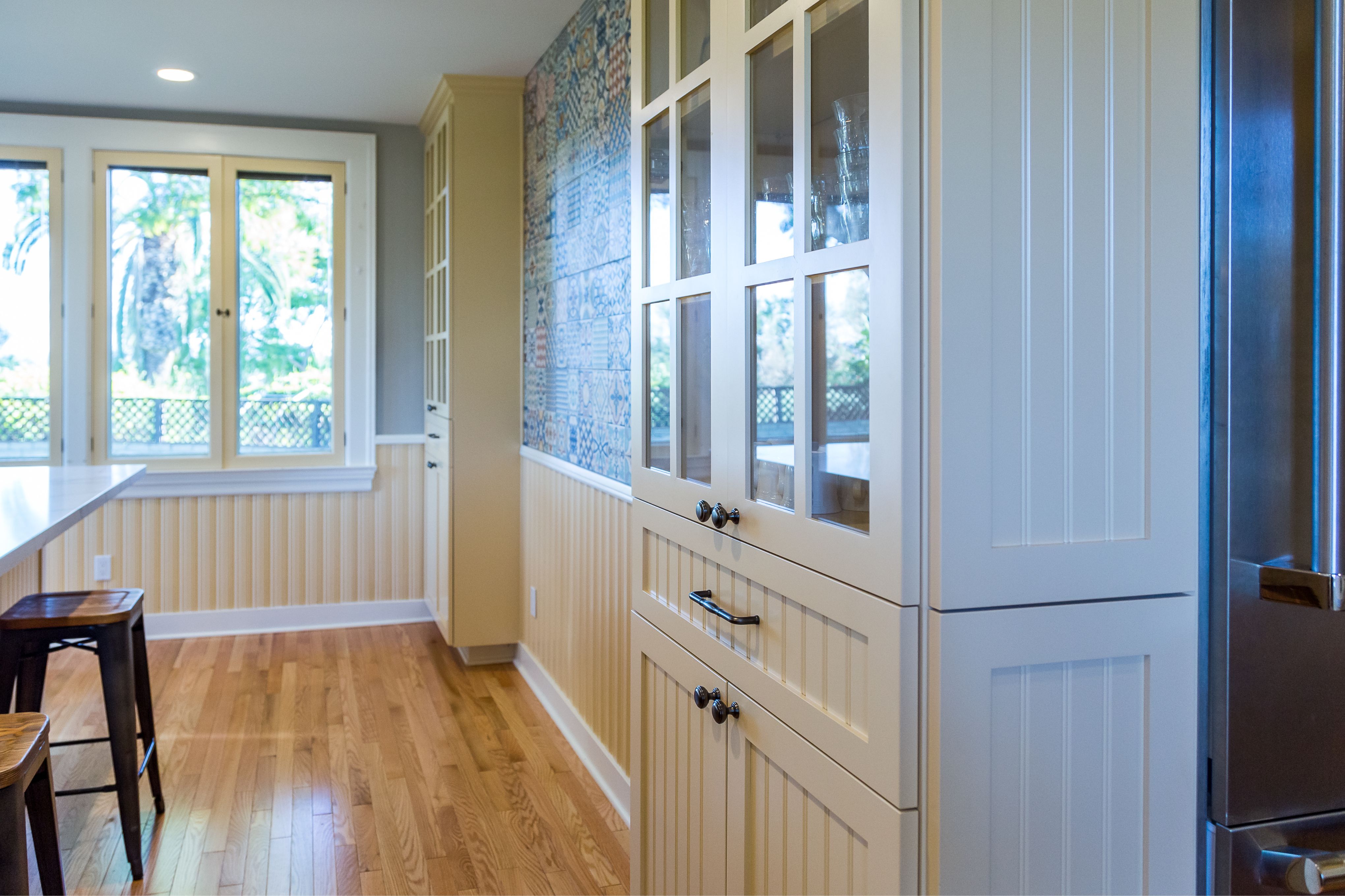 Kitchen with glass-front cream cabinetry, patterned tile accent wall, beadboard paneling and wood flooring