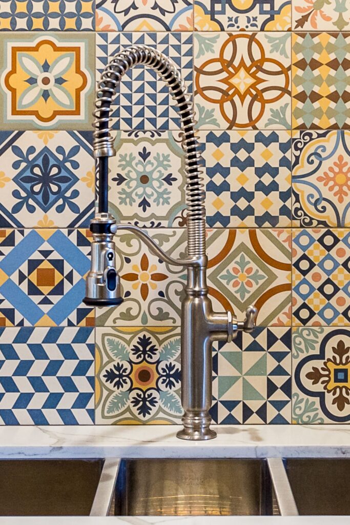 Spring-coil kitchen faucet over triple-basin stainless sink with colorful patterned tile backsplash