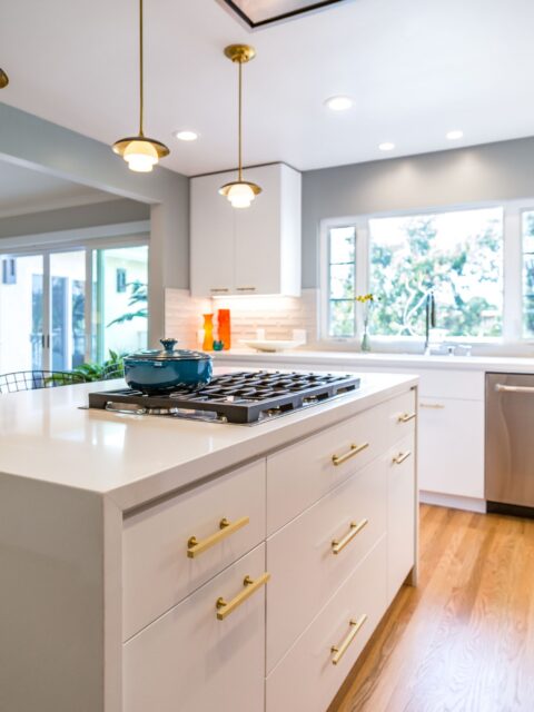 North Kensington kitchen island with gas cooktop, white cabinetry, brass hardware and pendant lighting