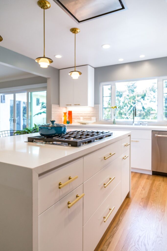 North Kensington kitchen island with gas cooktop, white cabinetry, brass hardware and pendant lighting