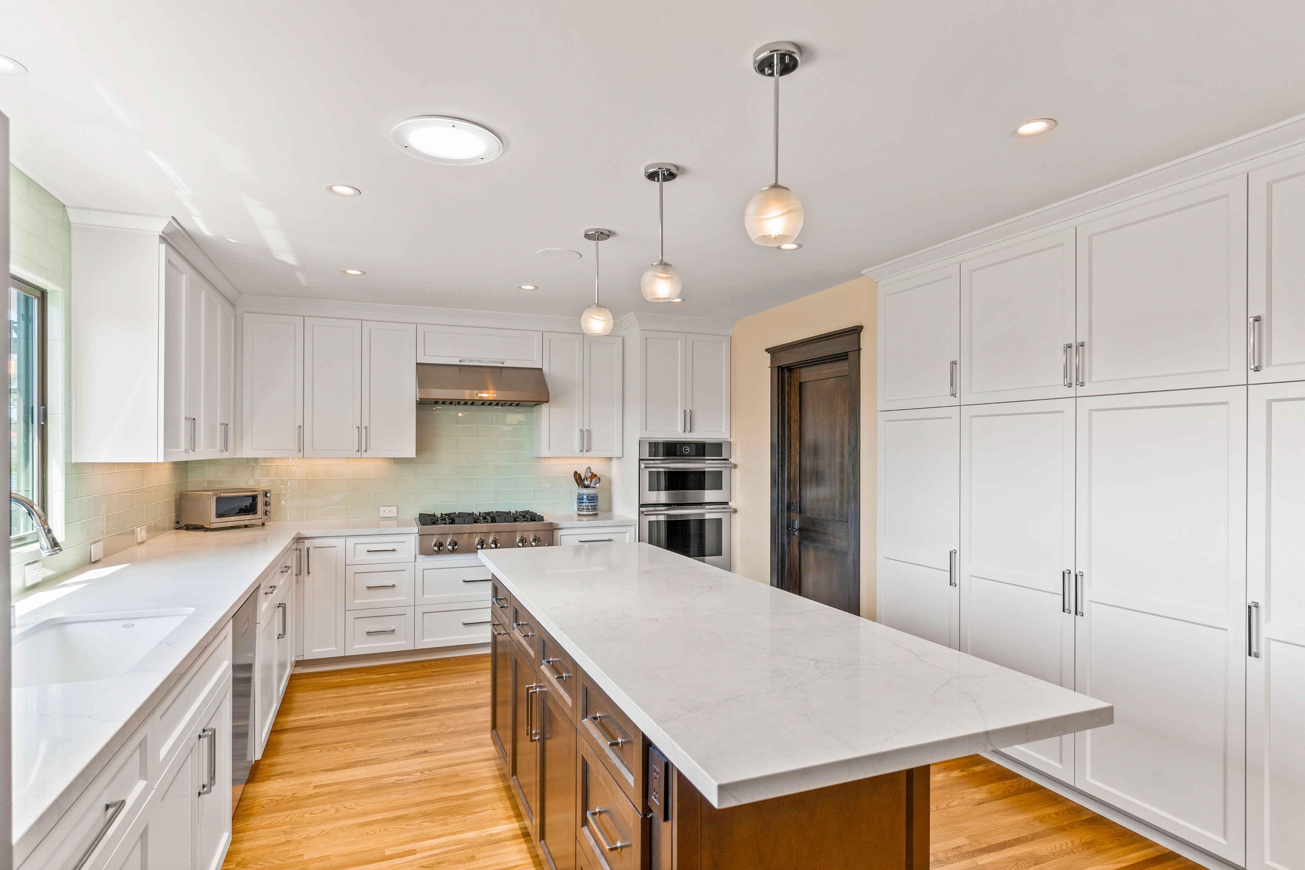 Remodeled kitchen with white cabinetry, dark wood island, quartz counters and pale green tile backsplash