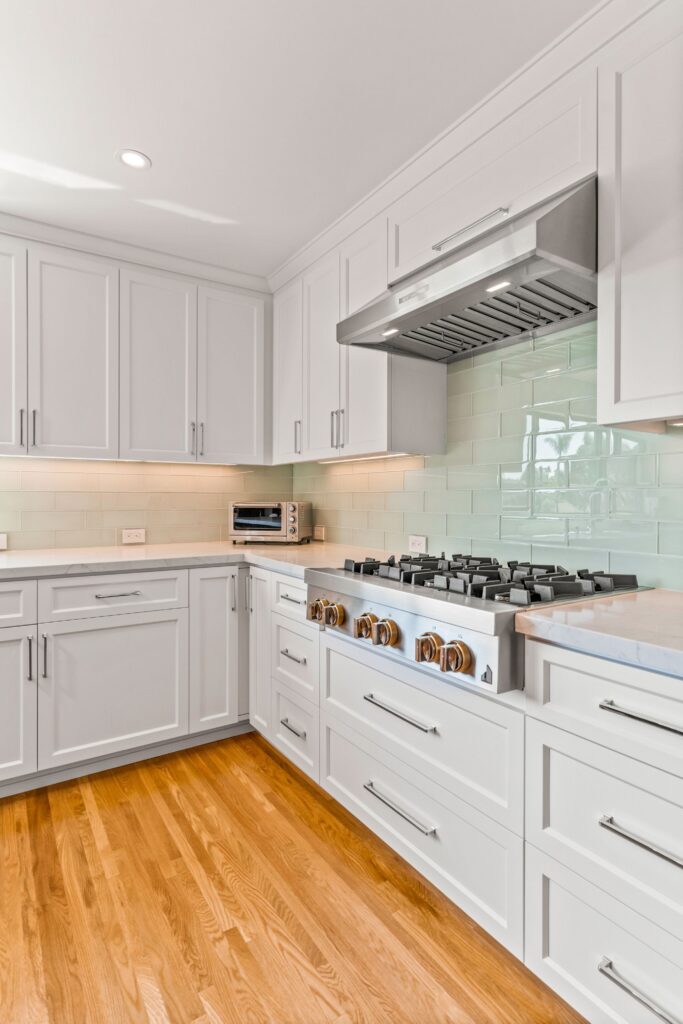 Kitchen range wall with white shaker cabinets, pale green subway tile, stainless hood and hardwood flooring