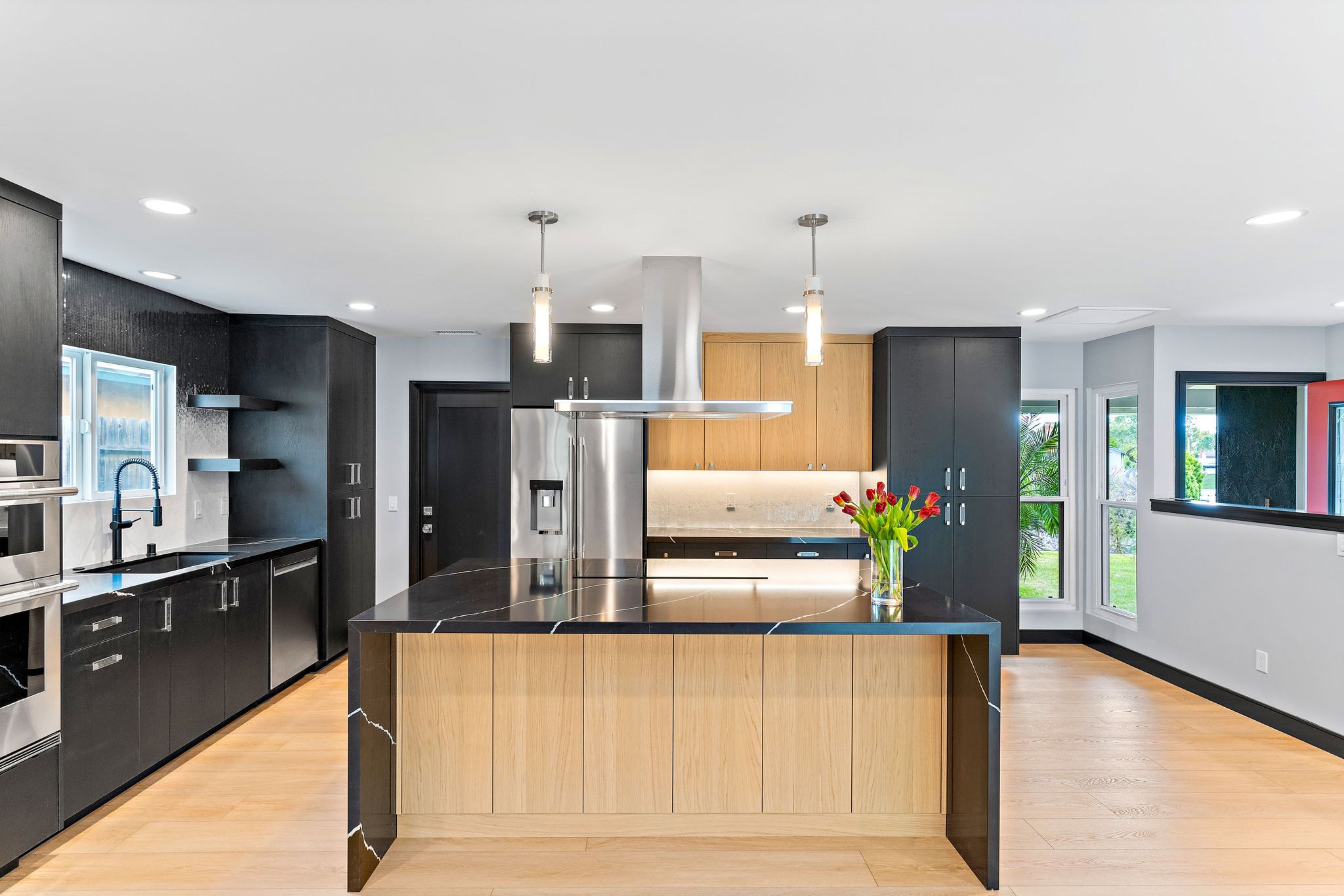 Contemporary kitchen with black waterfall island, wood cabinetry, stainless hood and pendant lighting