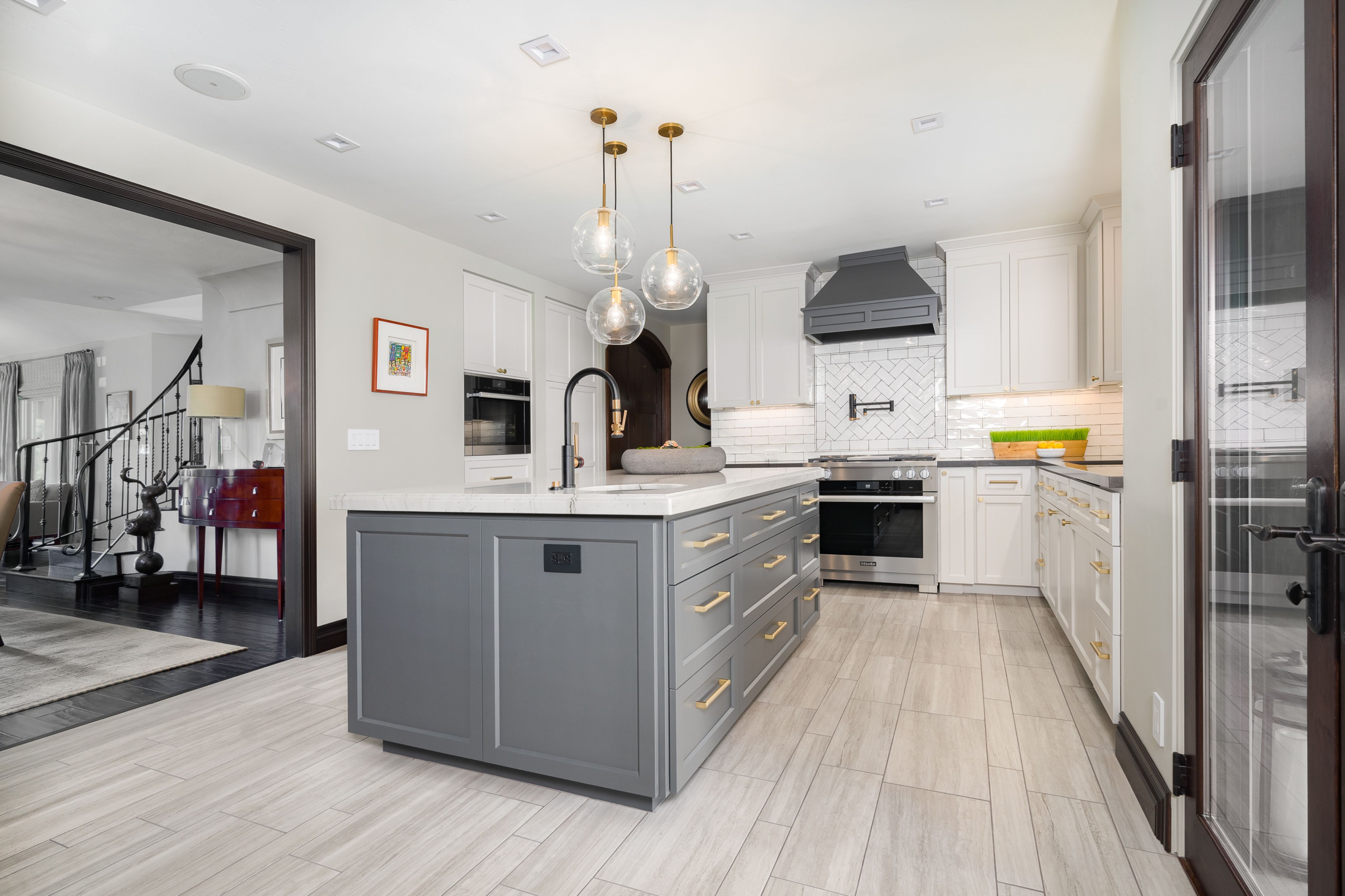 Wide kitchen with gray storage island, white cabinetry, glass pendants, stainless range and squared opening