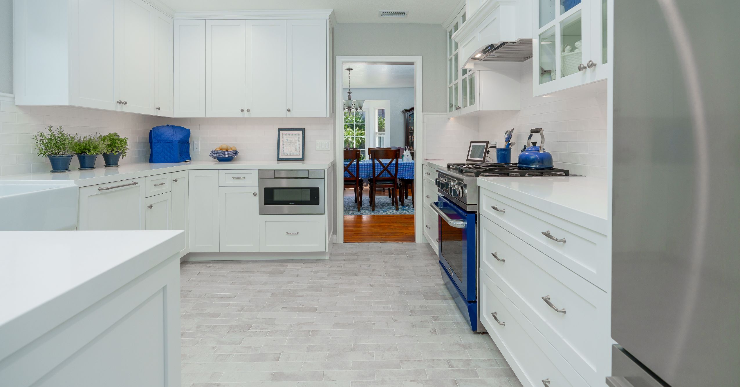 Bright white kitchen with farmhouse sink, shaker cabinets, quartz counters, and blue-accented range.