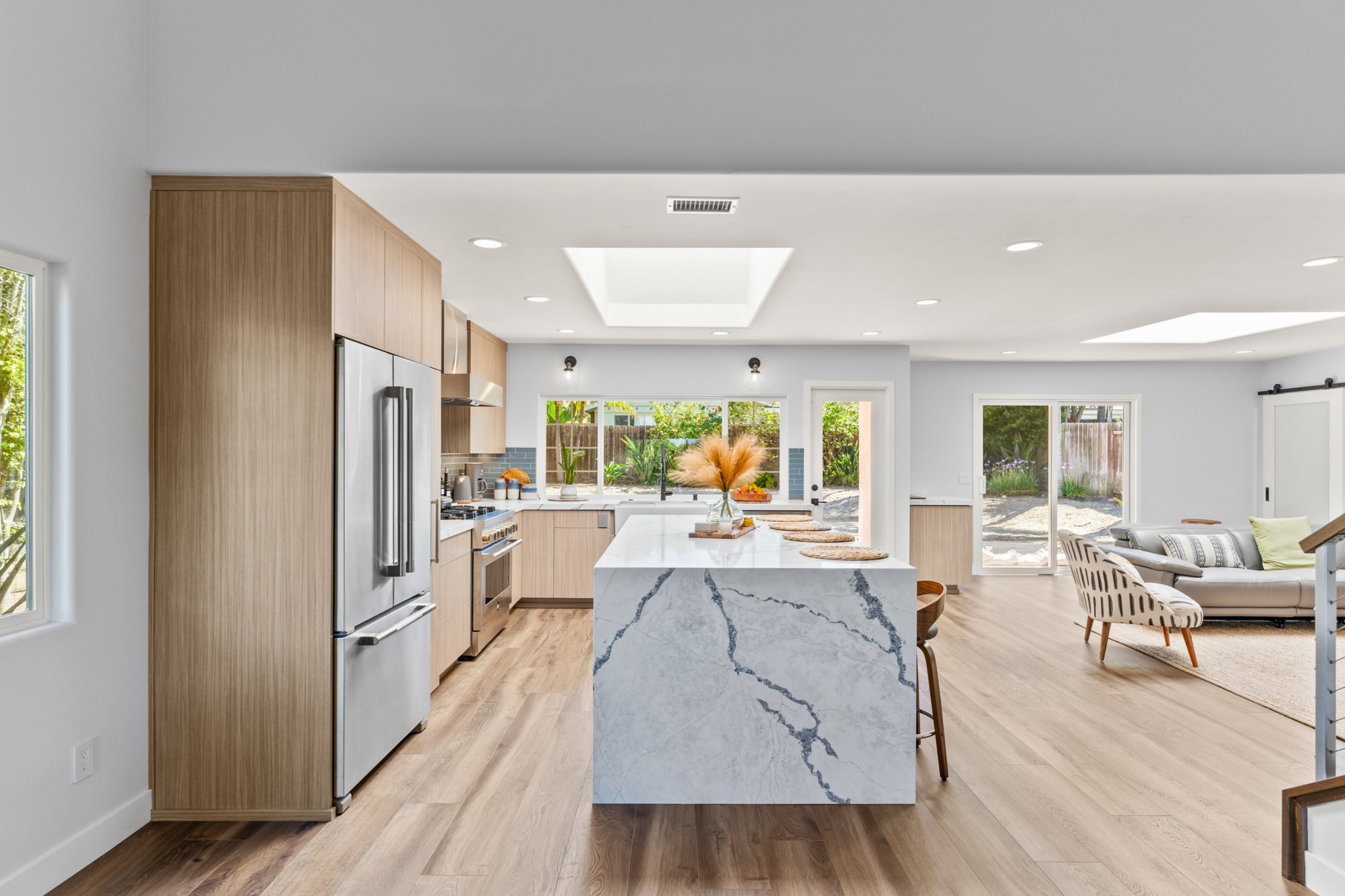 Light wood kitchen with waterfall island, stainless appliances, skylights and open connection to the family room.