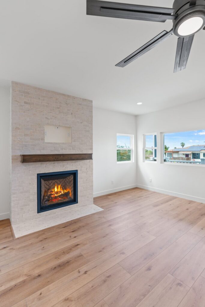 Second-floor living room with light wood flooring, tiled fireplace, wood mantel, ceiling fan and multiple windows.