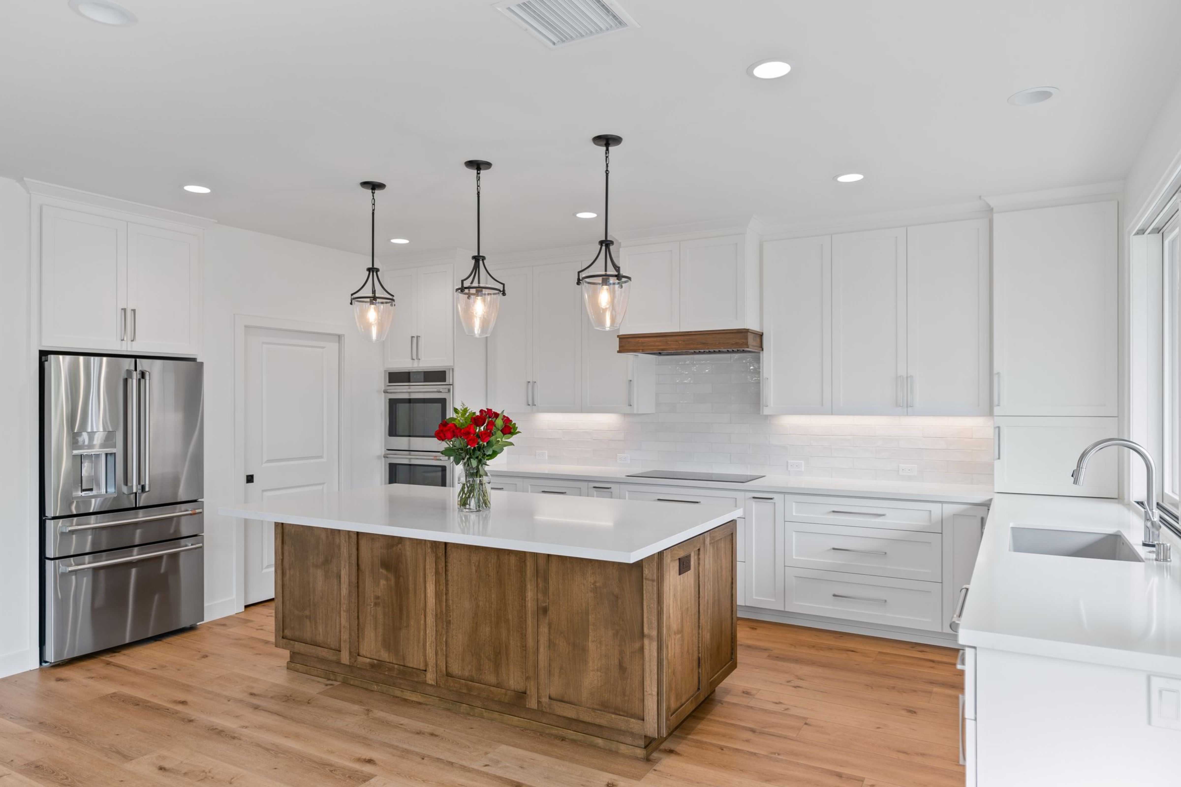 White kitchen with wood island, white counters, stainless appliances, pendant lights and wood hood trim.