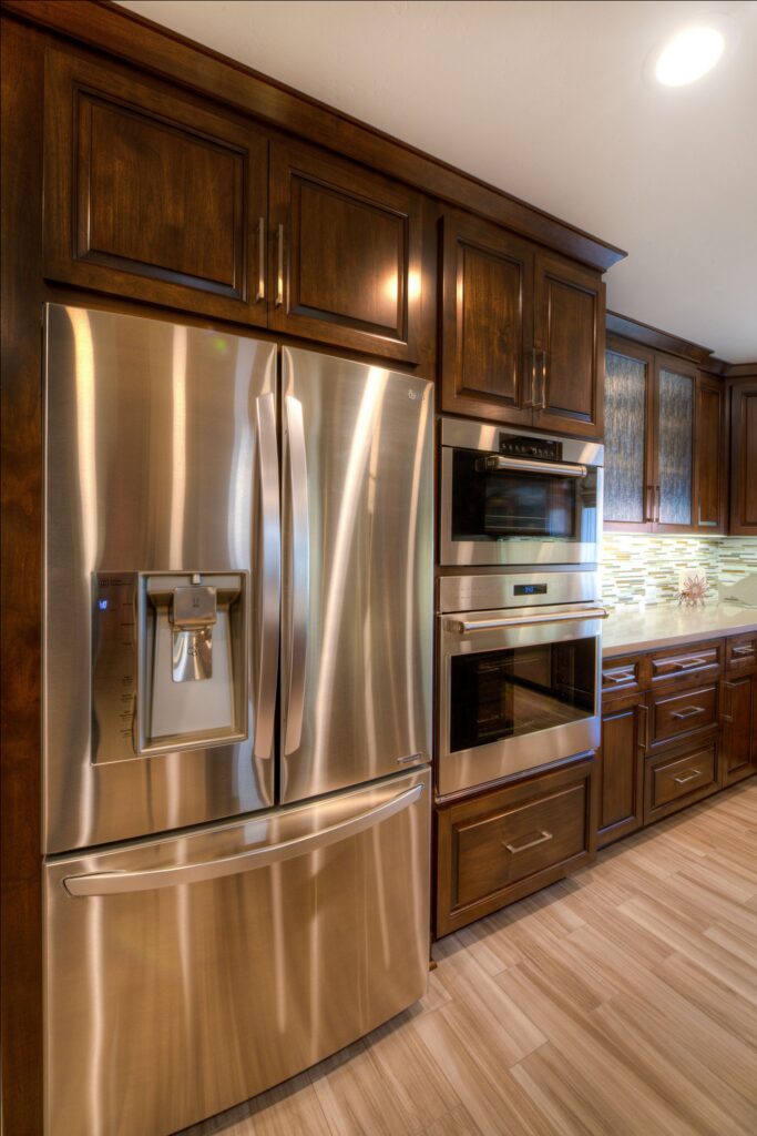 Stainless refrigerator and stacked wall ovens integrated into floor-to-ceiling dark wood kitchen cabinetry.