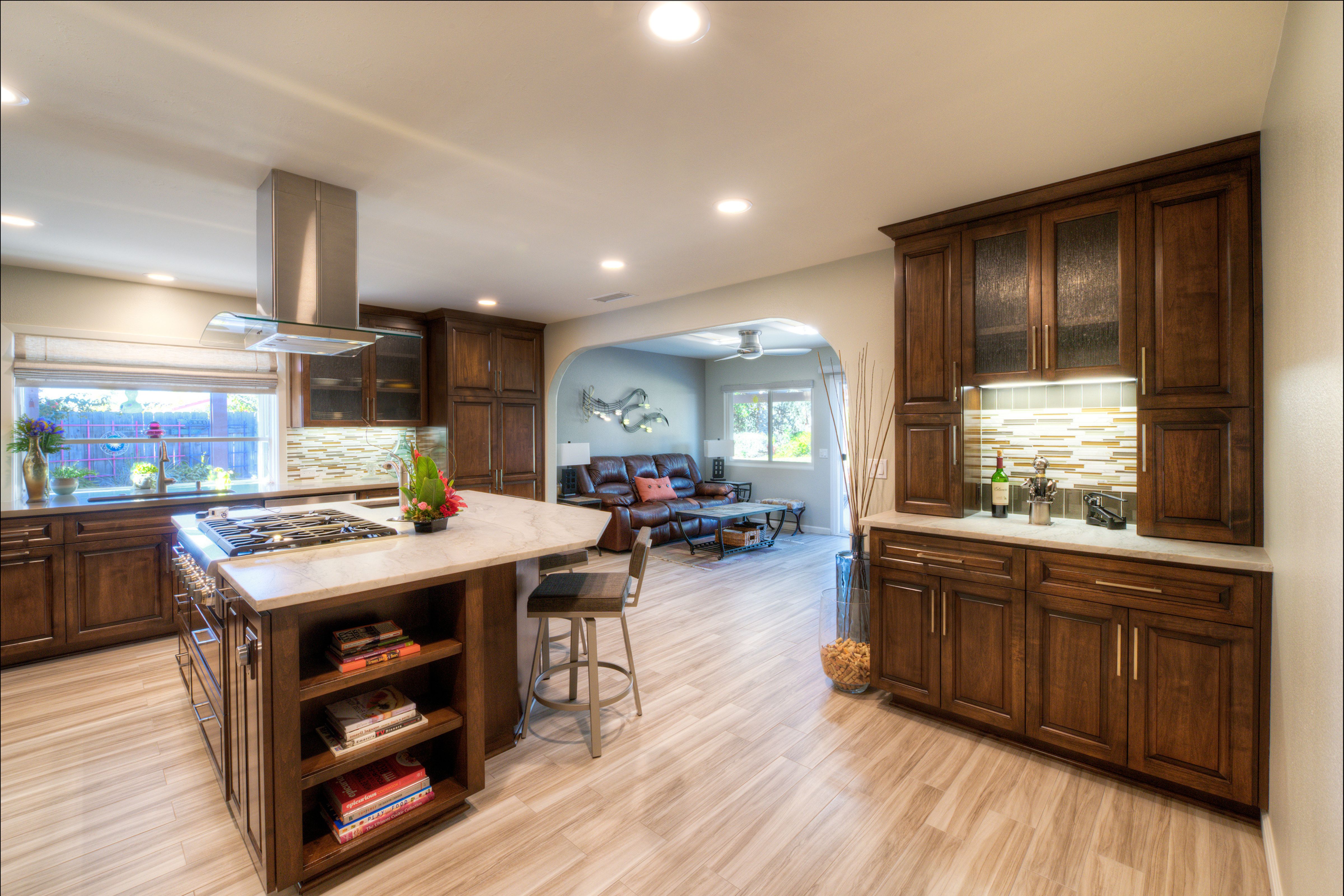 Mira Mesa kitchen remodel with large wood island, cooktop, glass hood, tall cabinetry and adjacent living area.