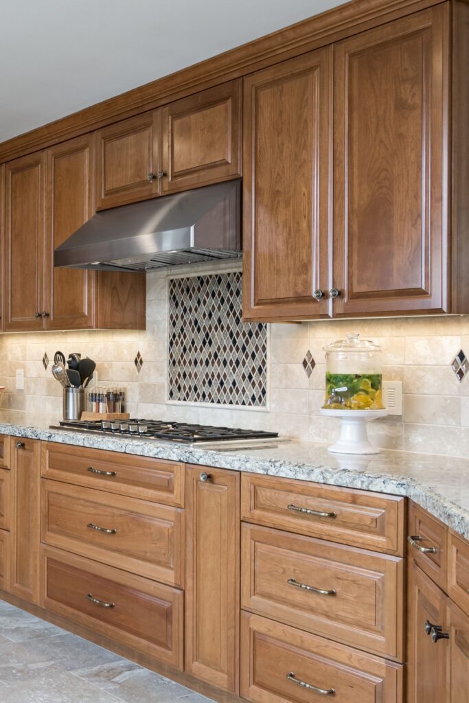 Kitchen cooktop wall with wood cabinetry, stainless steel hood, stone counter and diamond-accent tile backsplash