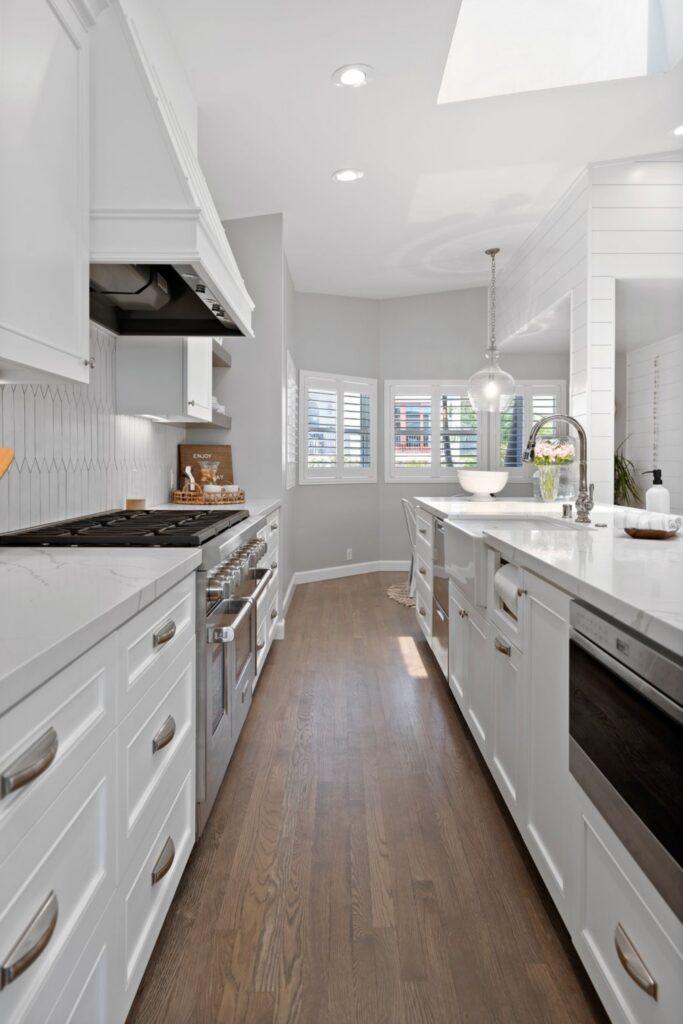 La Jolla kitchen with white cabinetry, wood flooring, quartz counters, stainless range, skylight and island sink