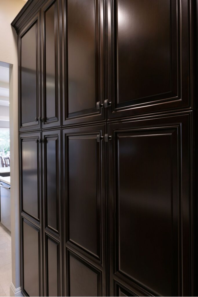 Floor-to-ceiling dark wood pantry cabinets with raised-panel doors and decorative hardware