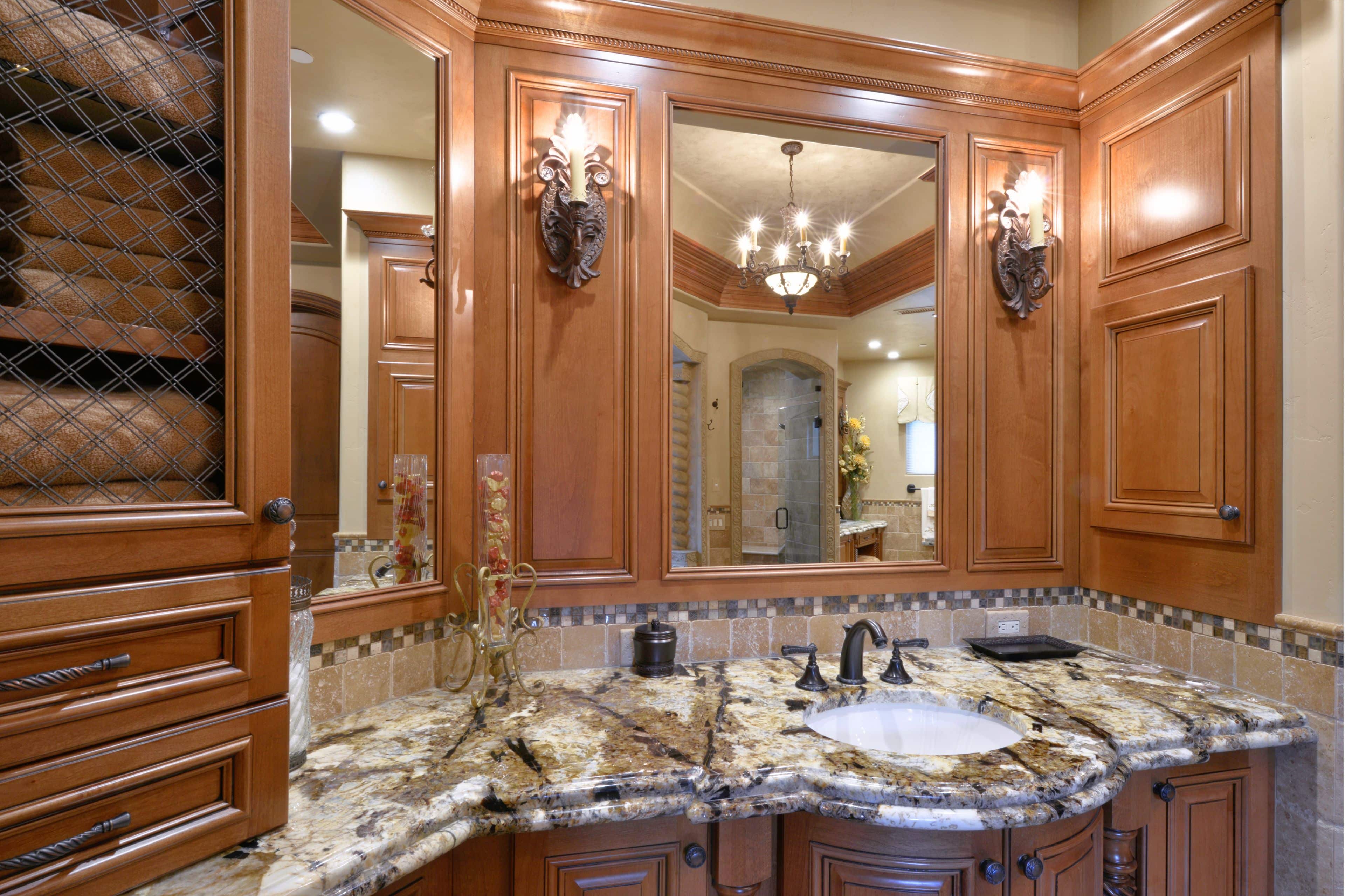 Custom wood bathroom vanity with stone countertop, inset sink, framed mirrors and decorative wall sconces.