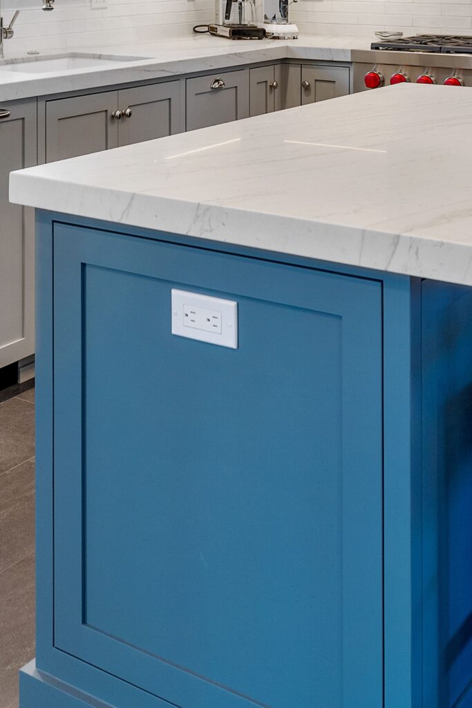 Blue kitchen island end panel with integrated electrical outlet beneath a thick white solid-surface countertop.