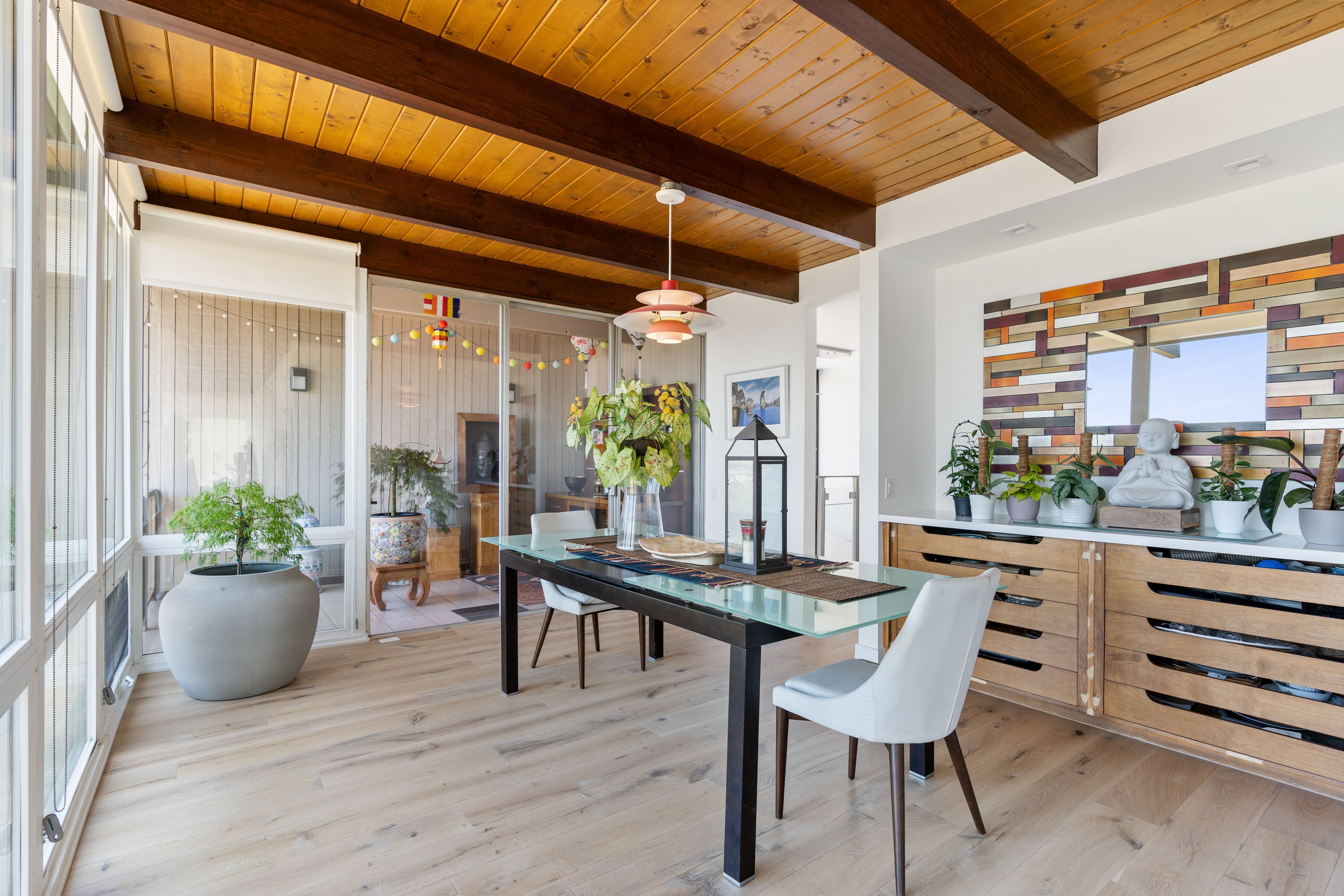 Dining room with exposed wood beam ceiling, wide windows, wood flooring, glass table and built-in storage.