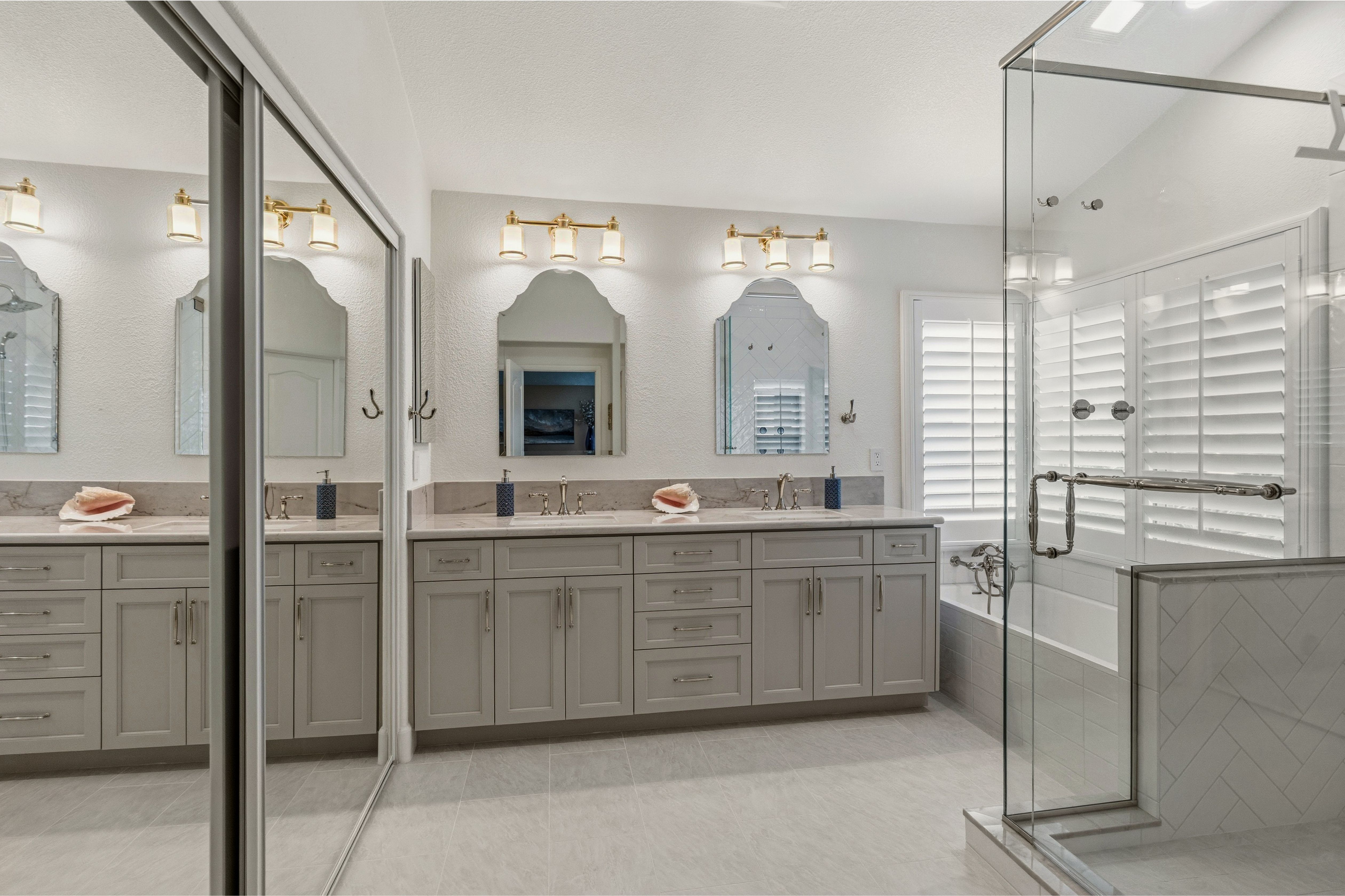 Primary bath with a long double vanity, large-format tile, decorative mirrors and a glass shower enclosure.
