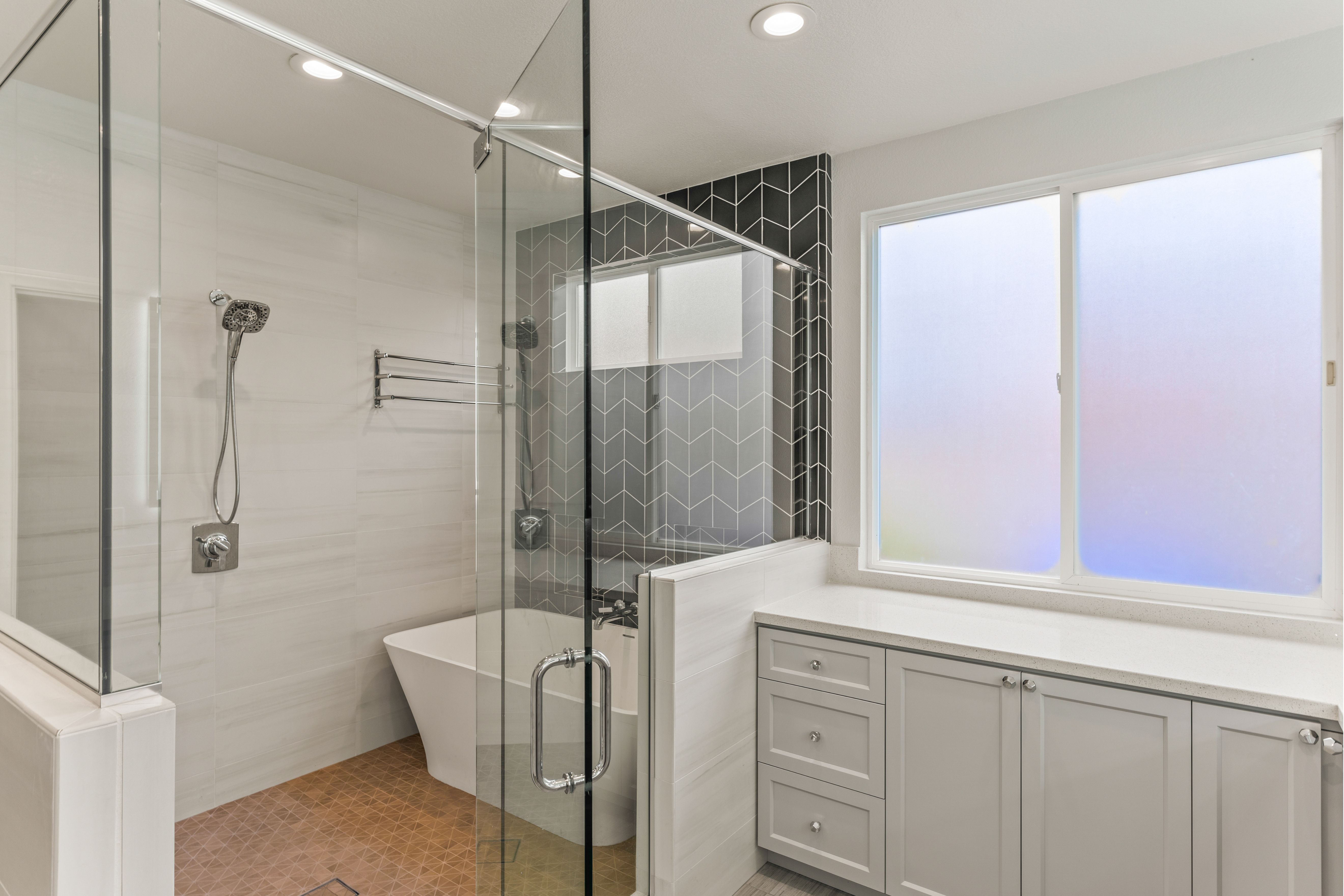 Bathroom with glass shower, freestanding tub, frosted windows and built-in gray storage cabinetry.