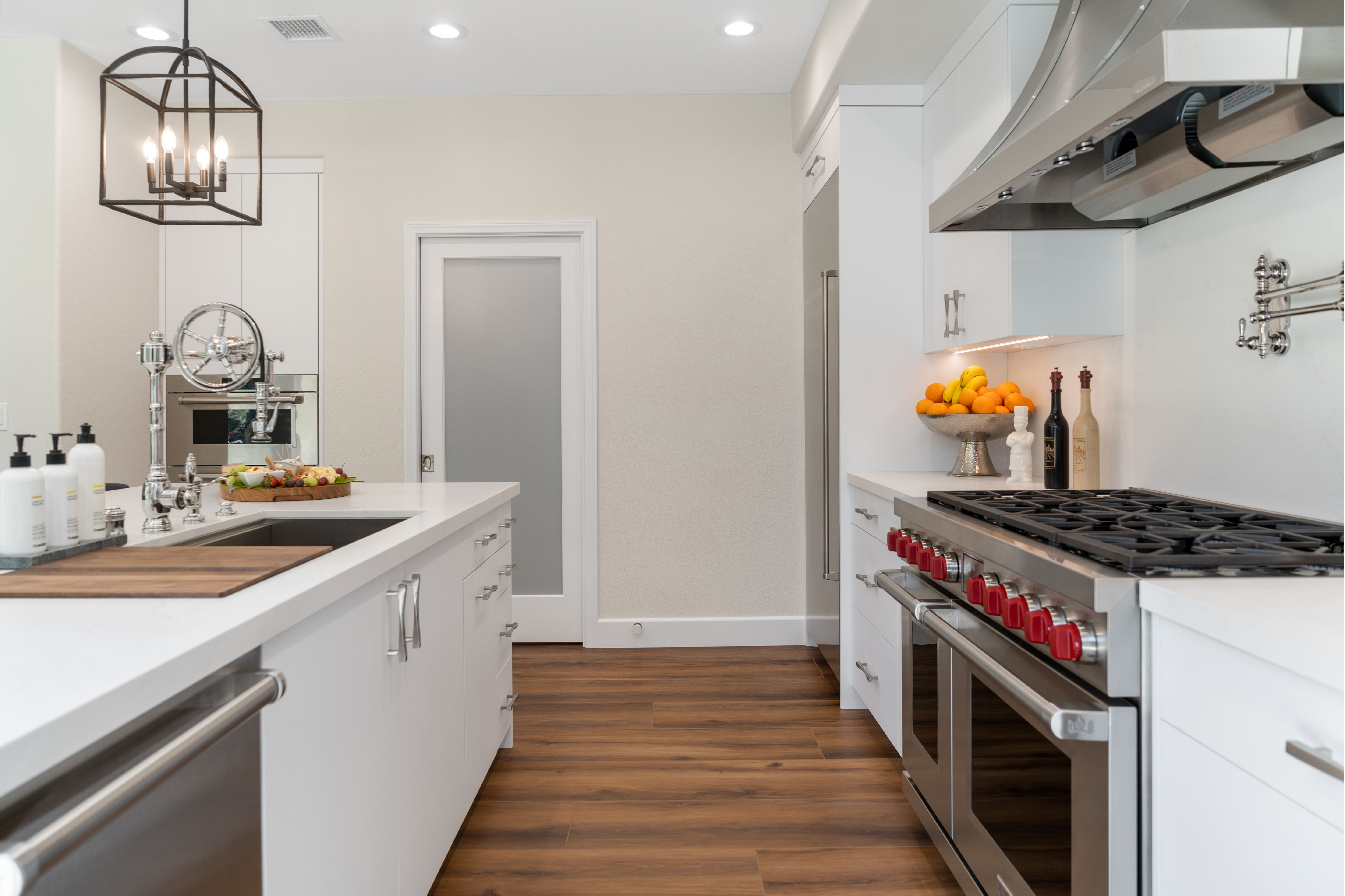 Kitchen work aisle with white cabinetry, large stainless range, pot filler, island sink and wood-look flooring.