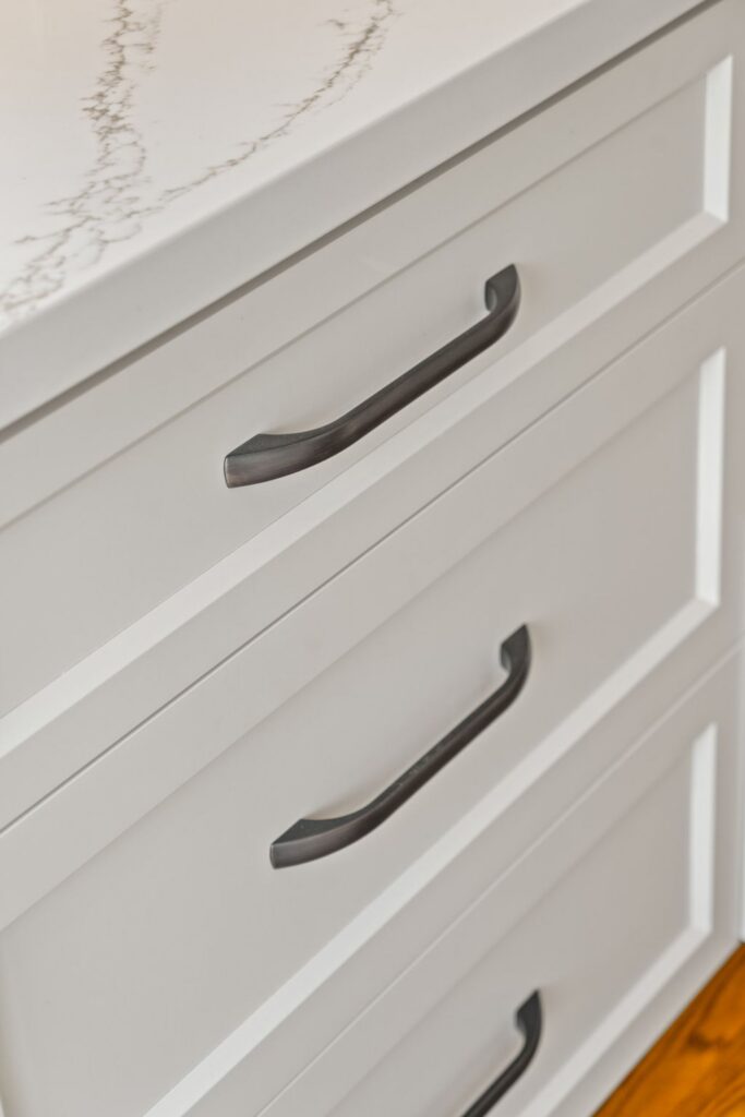 Close-up of white shaker-style kitchen drawers with dark metal pulls beneath a veined countertop.
