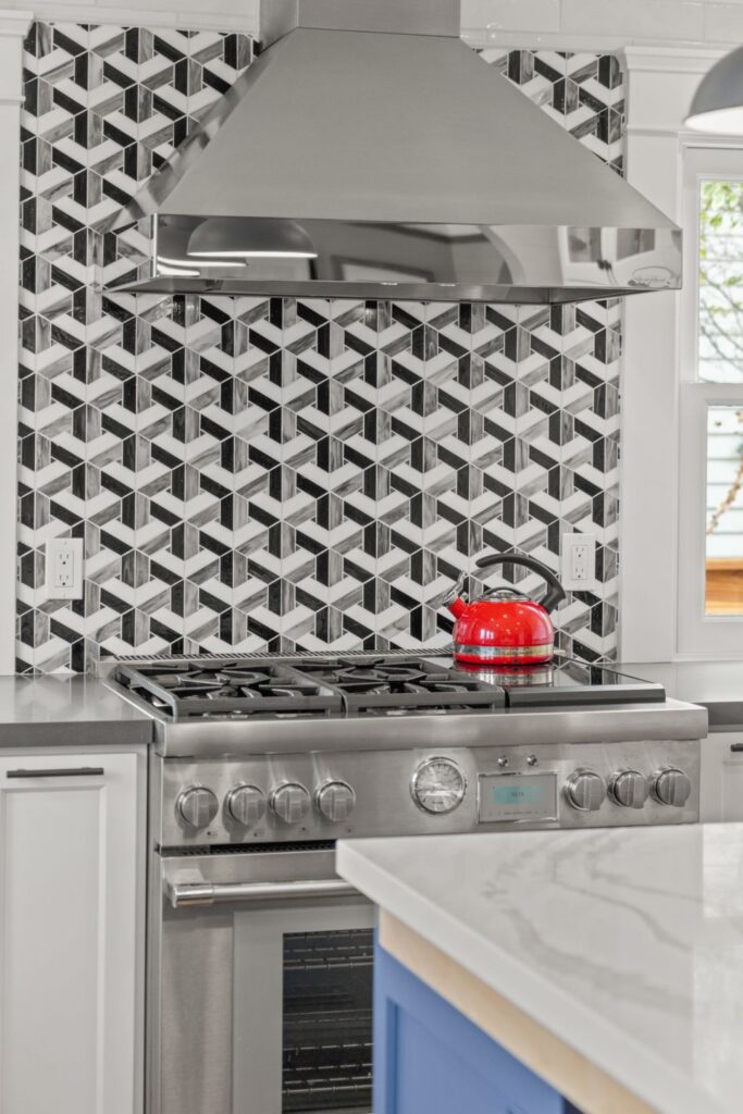 Stainless range and vent hood framed by a black-and-white geometric backsplash beside the blue kitchen island.