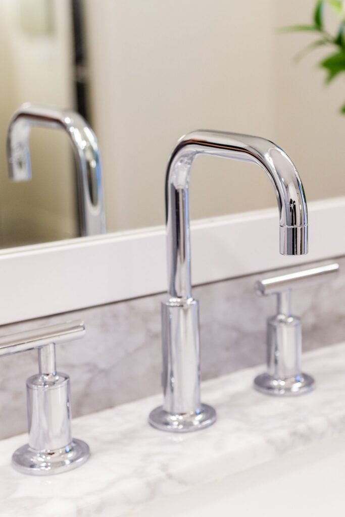 Chrome bathroom faucet and handles set into a light veined stone vanity beneath a framed mirror.